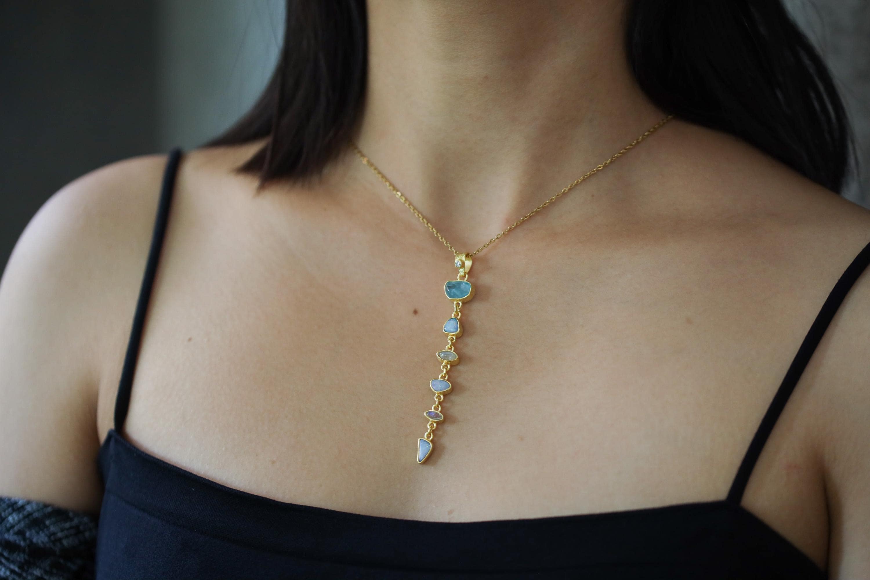 Vertical Aquamarine Opal Moonstone pendant shown worn on a model, with 18k gold-plated sterling silver and luminous blue stones.