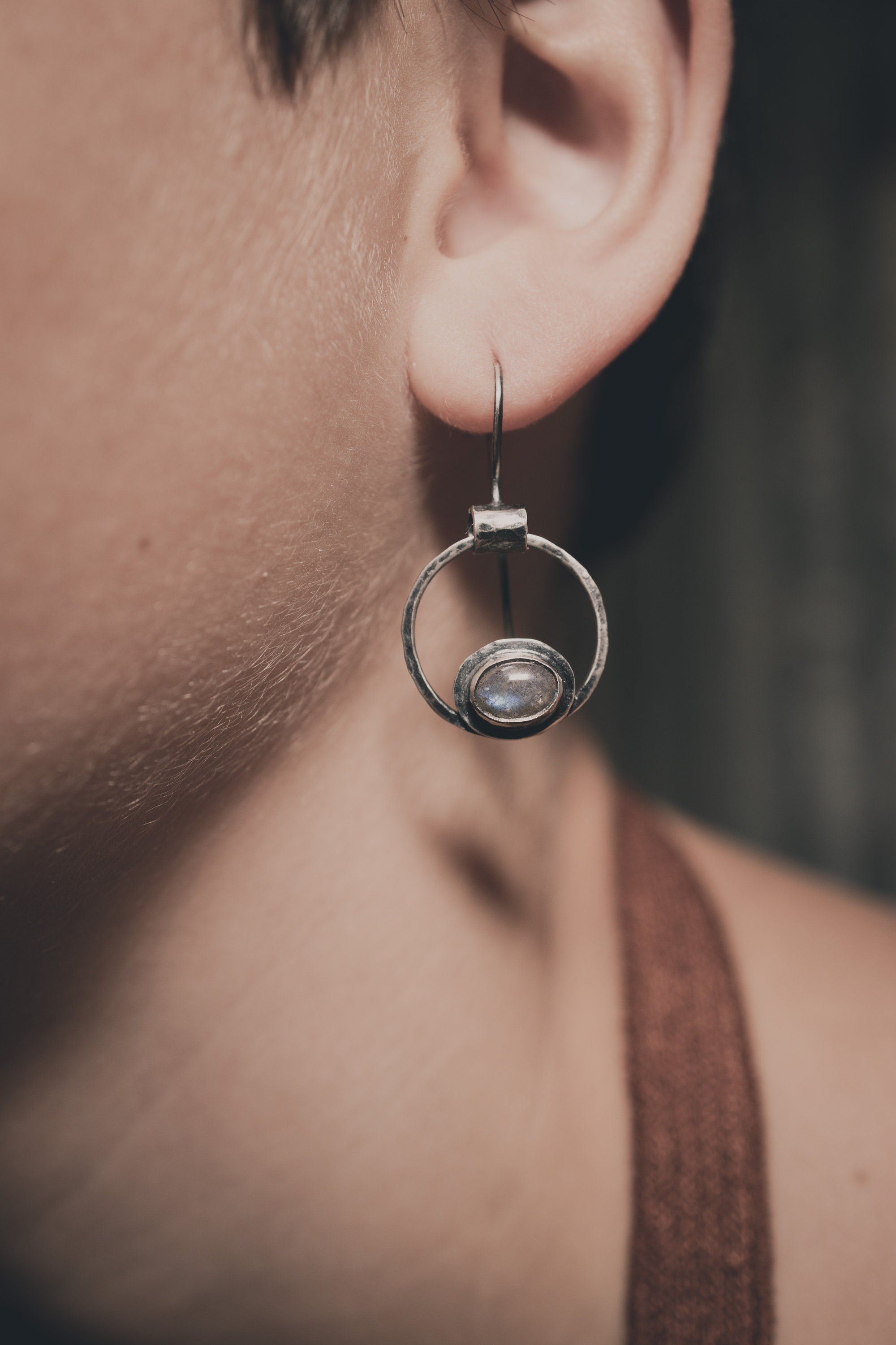 Old World Labradorite Cat Eye earrings in hammered 925 sterling silver shown worn on the ear with circular dangle form.