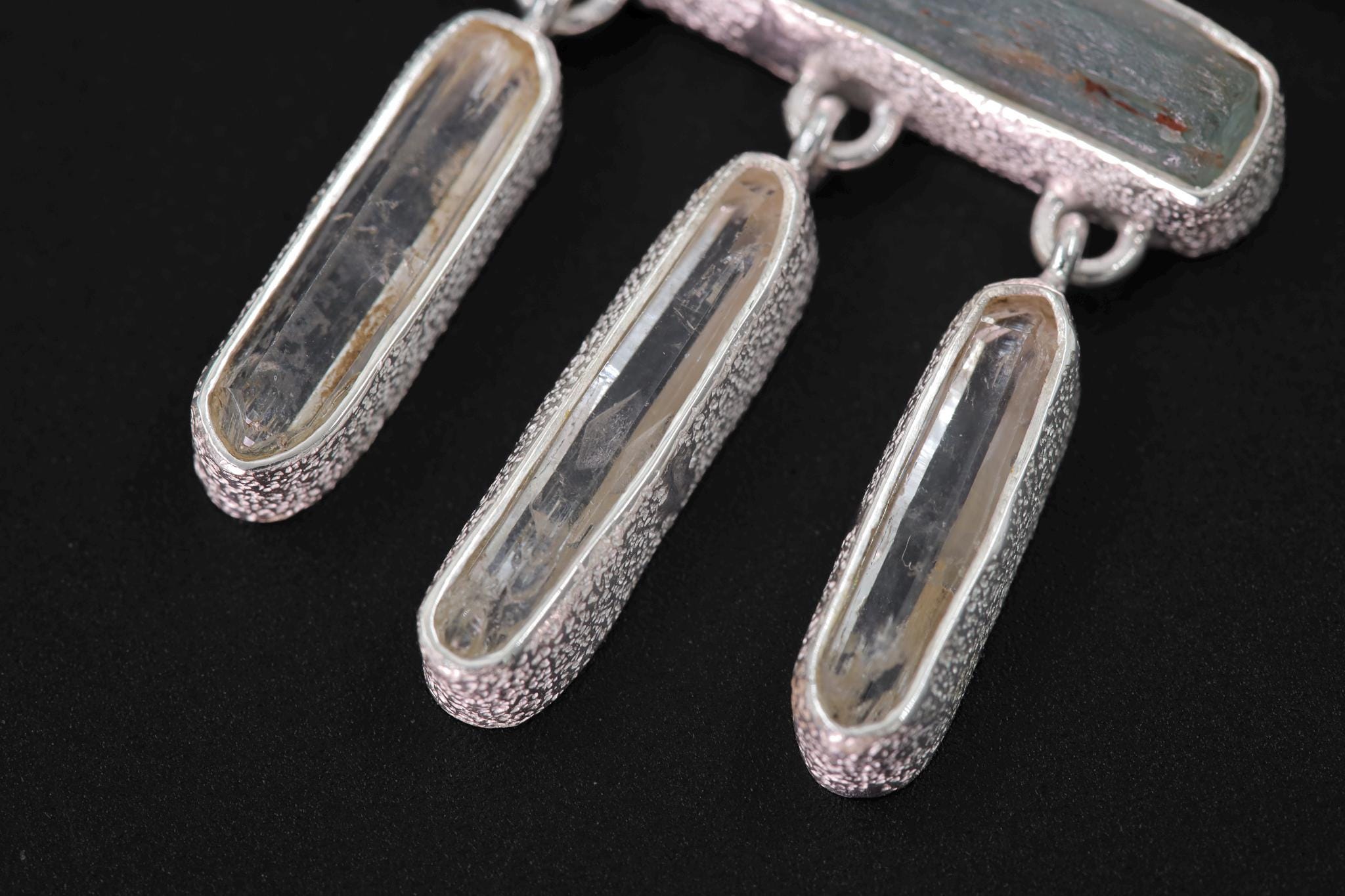 Close-up of Clear Quartz dangles beneath Red Kyanite and Aquamarine in an organic textured sterling silver pendant.