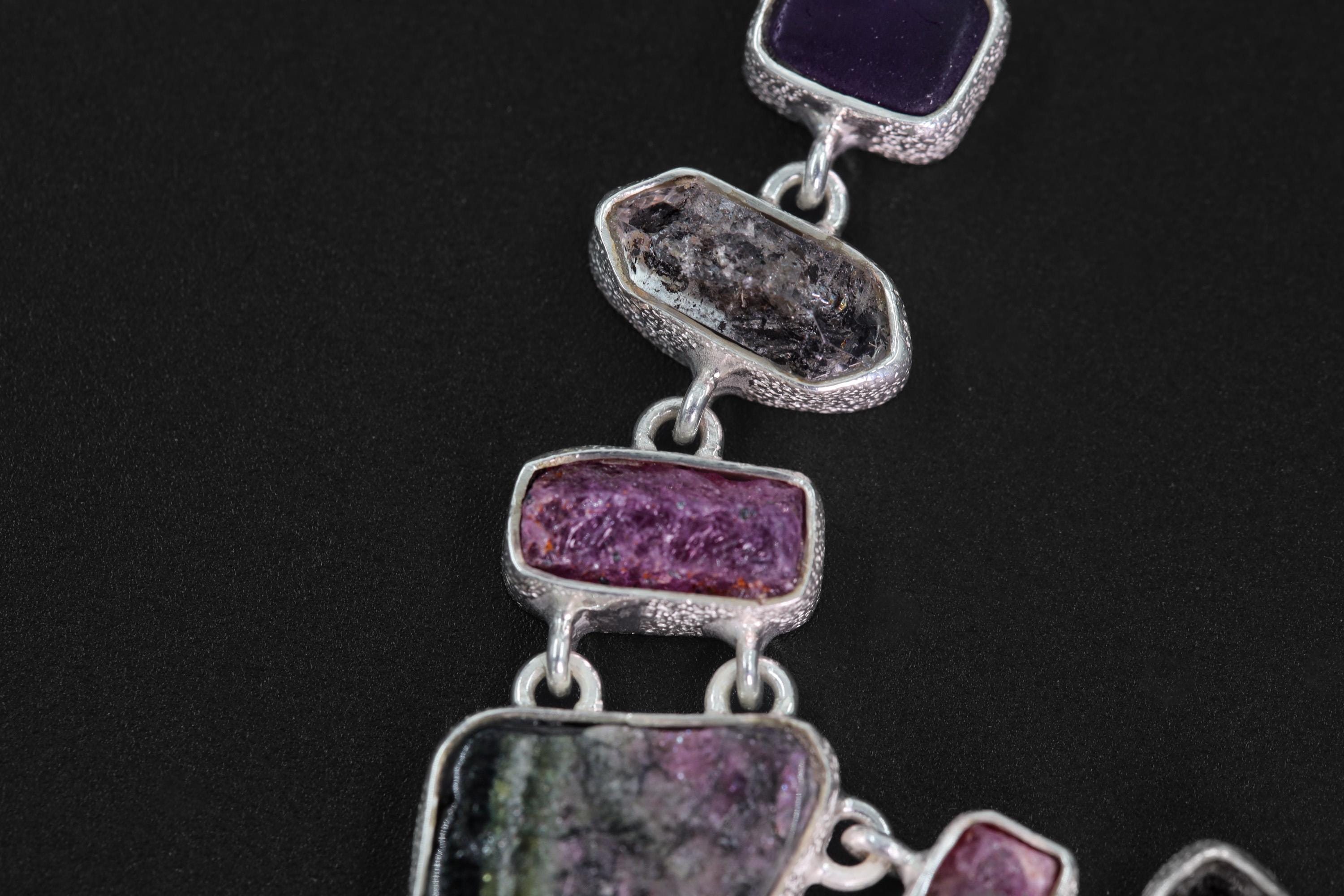 Close-up of raw Ruby and Green Tourmaline stones in a sterling silver multi-stone linked talisman necklace.