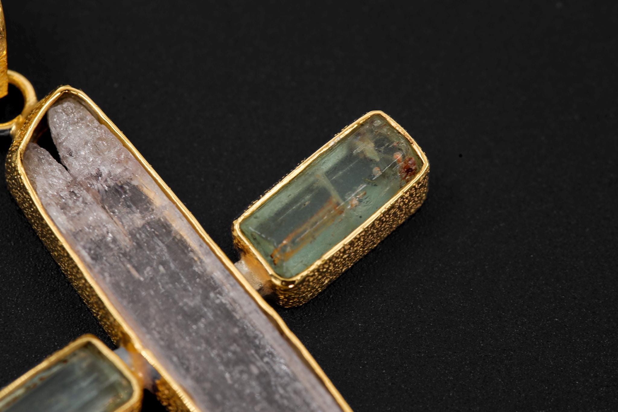 Close-up of Aquamarine side crystal and Pink Kunzite centre stone in an organic textured gold-plated cross pendant.