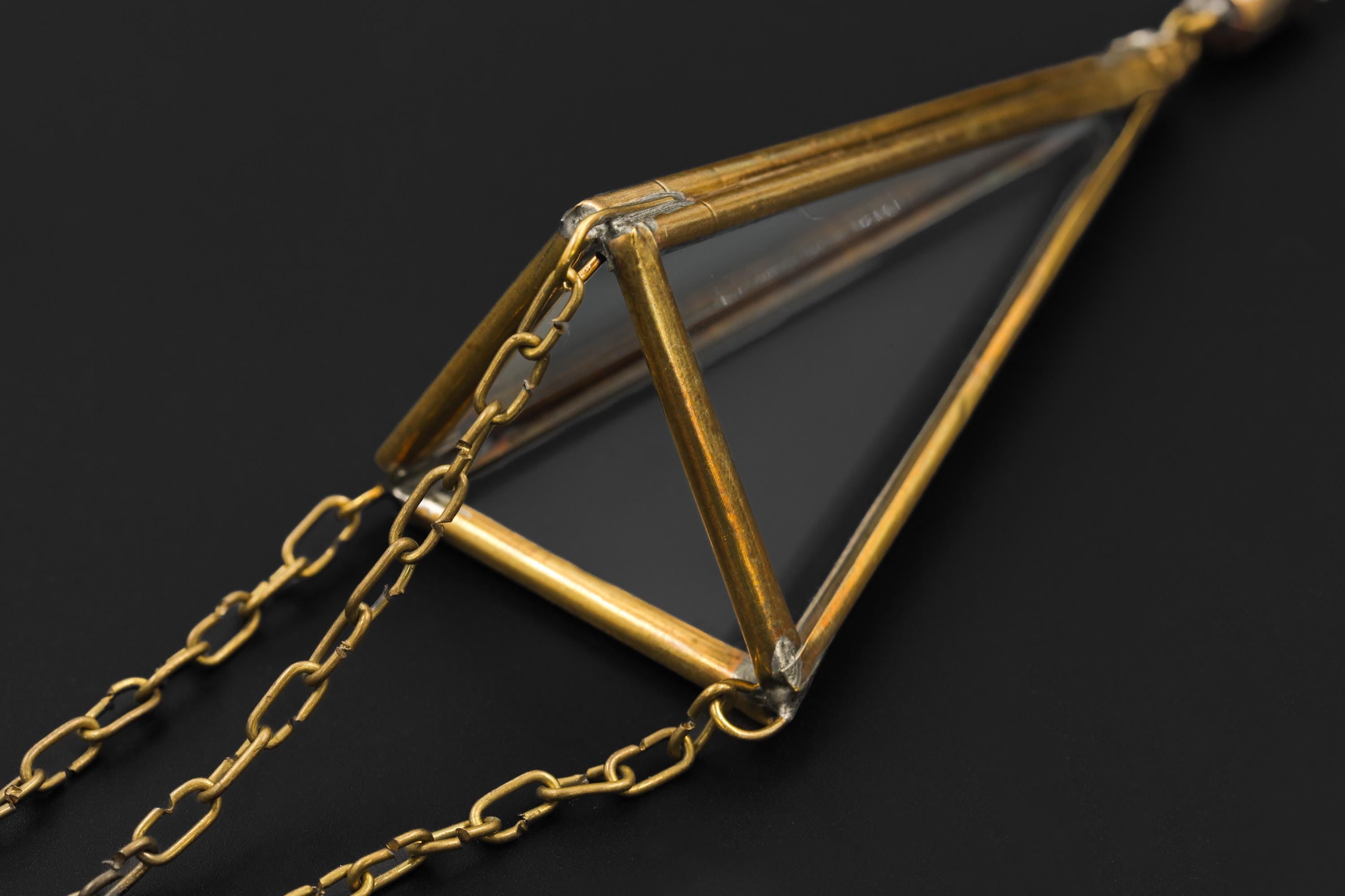 Close-up of brass and glass triangle prism sun catcher showing Clear Quartz point and warm metal frame.