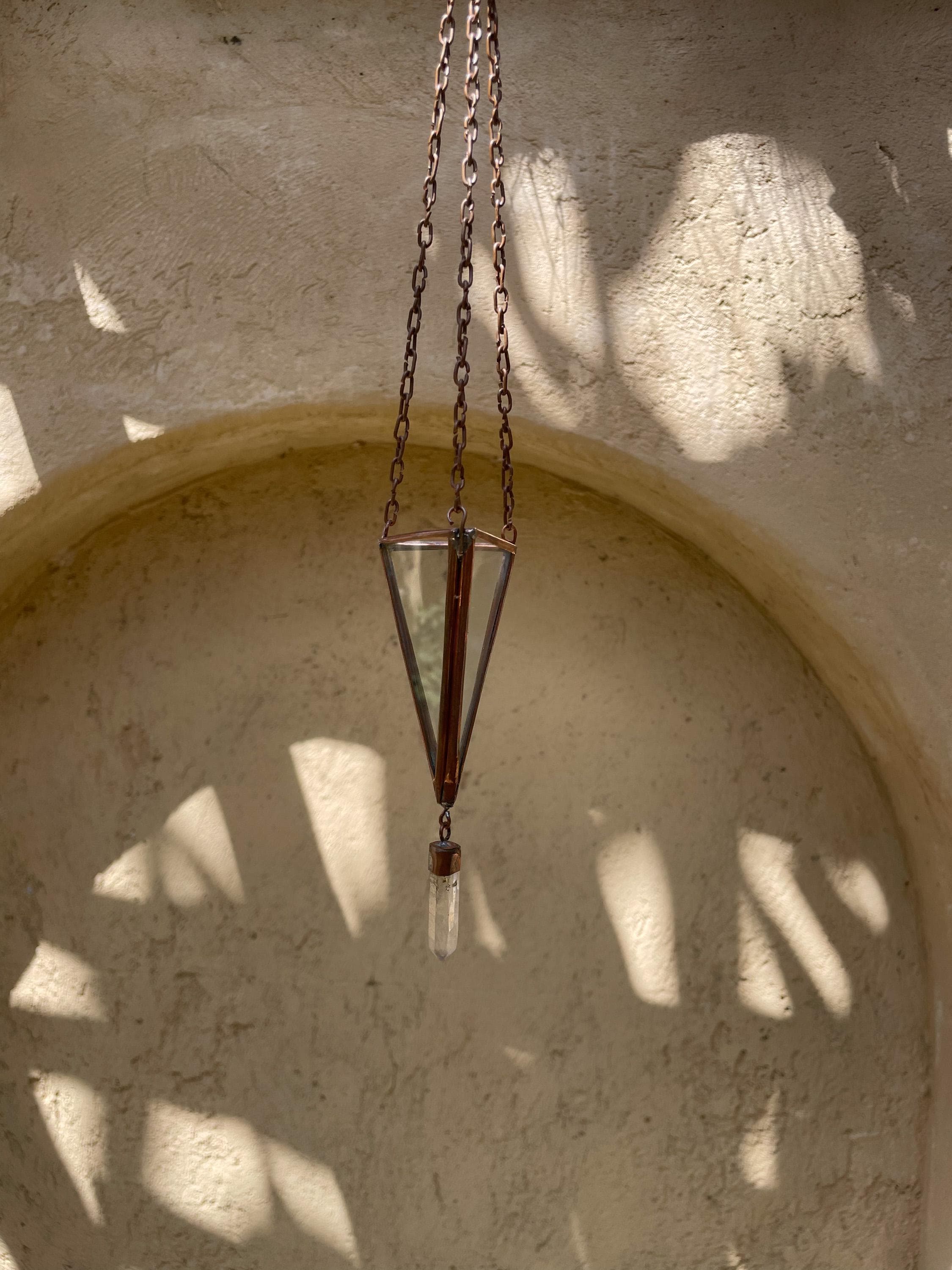 Copper Quartz triangle sun catcher hanging on textured wall with soft natural light and crystal point.