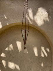 Copper Quartz triangle sun catcher hanging on textured wall with soft natural light and crystal point.