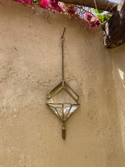 Quartz Reliquary mirror wall hanging shown in sunlight with geometric brass frame and suspended crystal point.