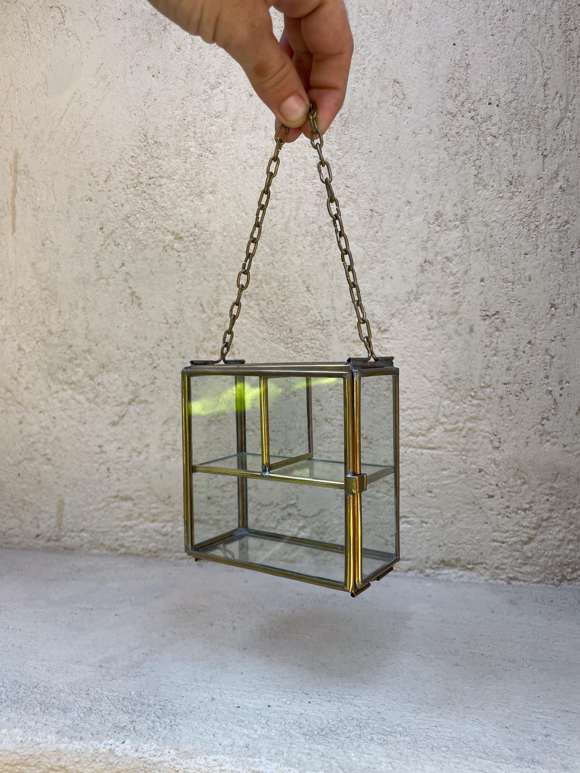 Large brass glass display box held by chain, showing rectangular shape and two-level interior shelf.
