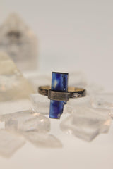 Raw Kyanite sterling silver ring displayed on clear quartz, with deep blue blade crystal and oxidized hammered band.