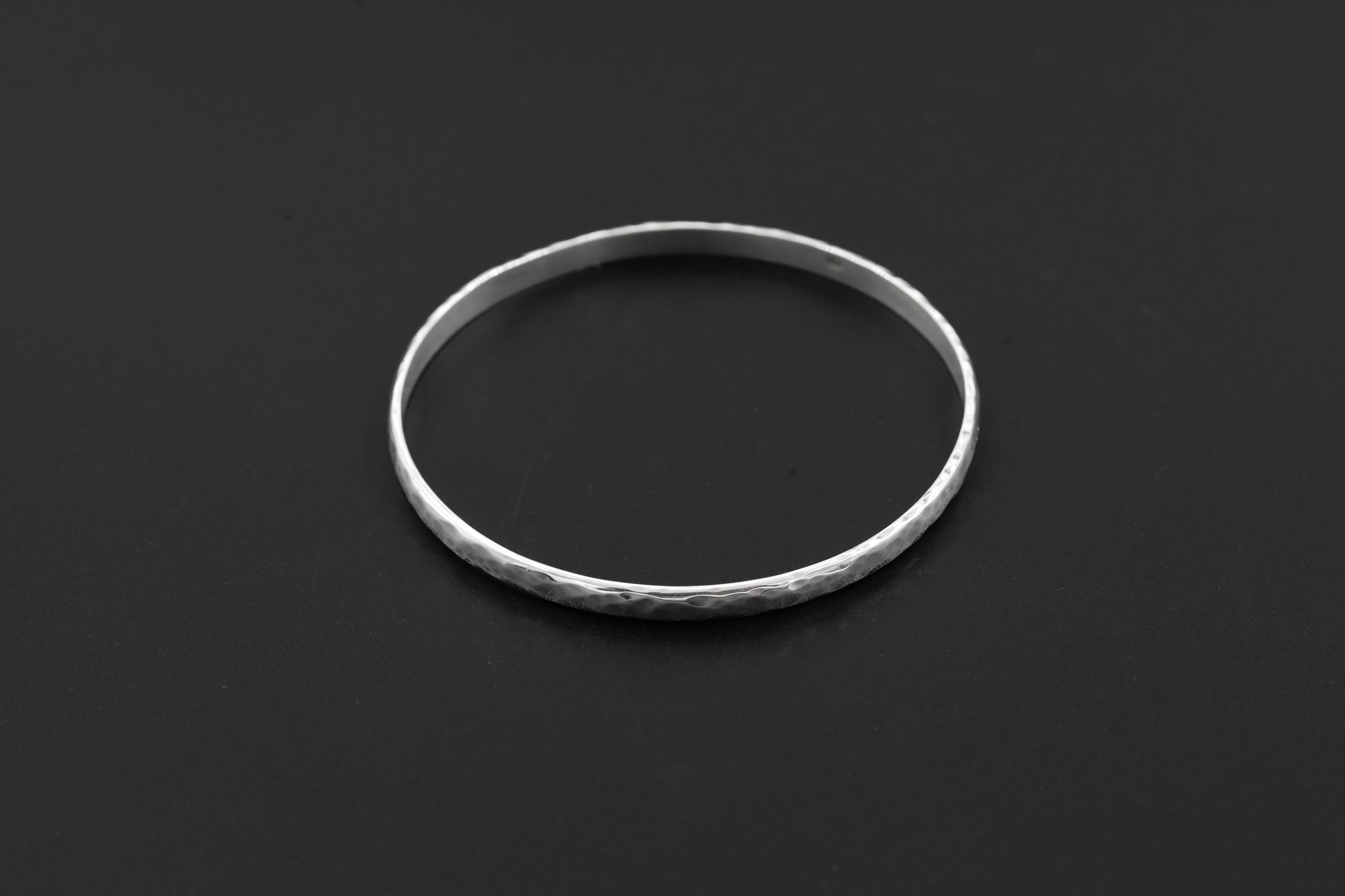 Hammered sterling silver bangle displayed on black background with clean circular shape.