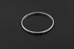 Hammered sterling silver bangle displayed on black background with clean circular shape.