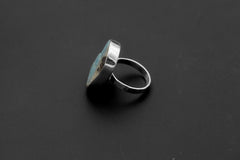 Side view of handmade Larimar ring showing raised freeform stone, polished bezel, and hammered sterling silver band.