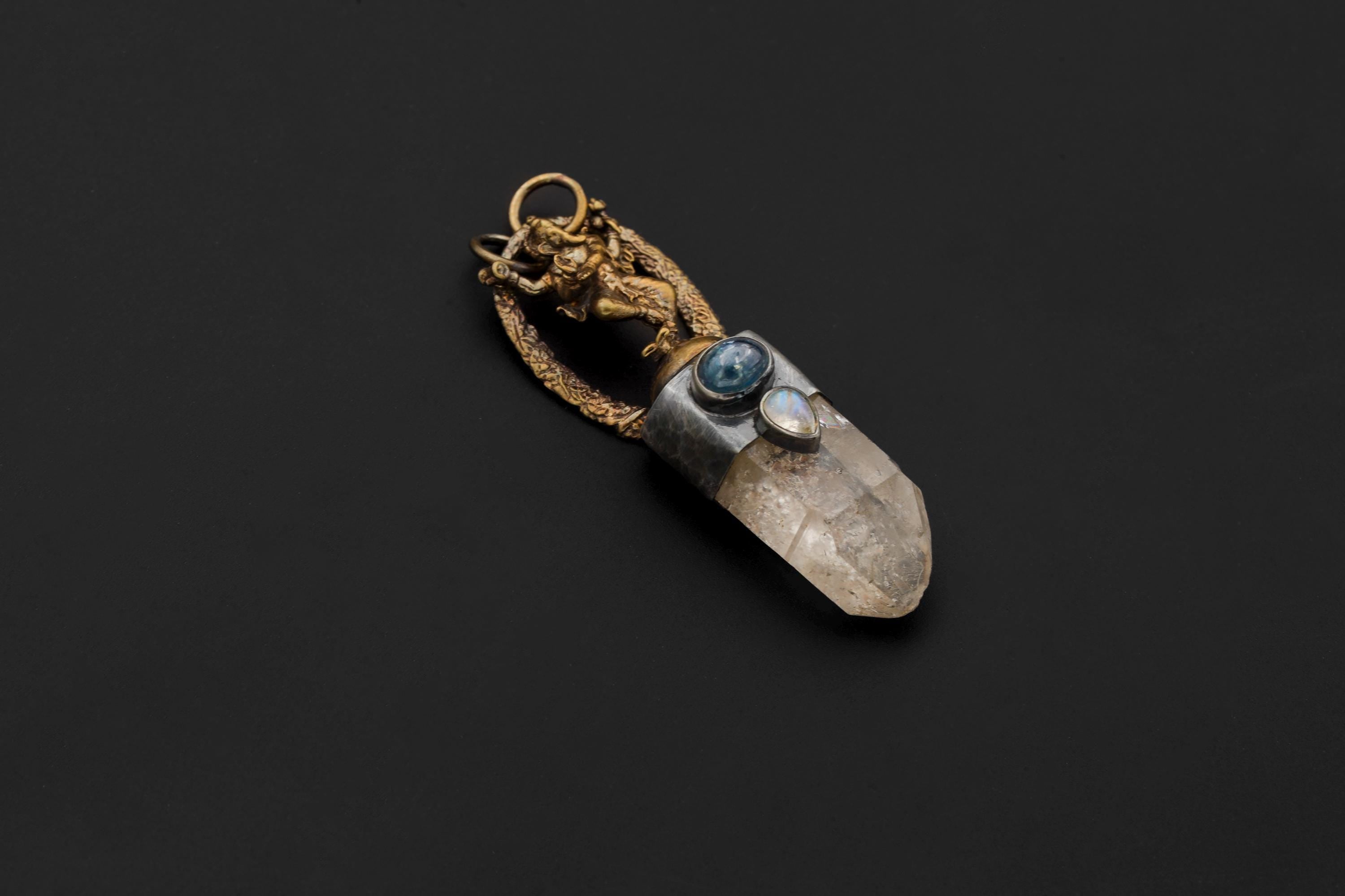 Overhead flat lay of pendant displaying Ganesha figure, quartz clarity, and gold-toned oxidized finish.