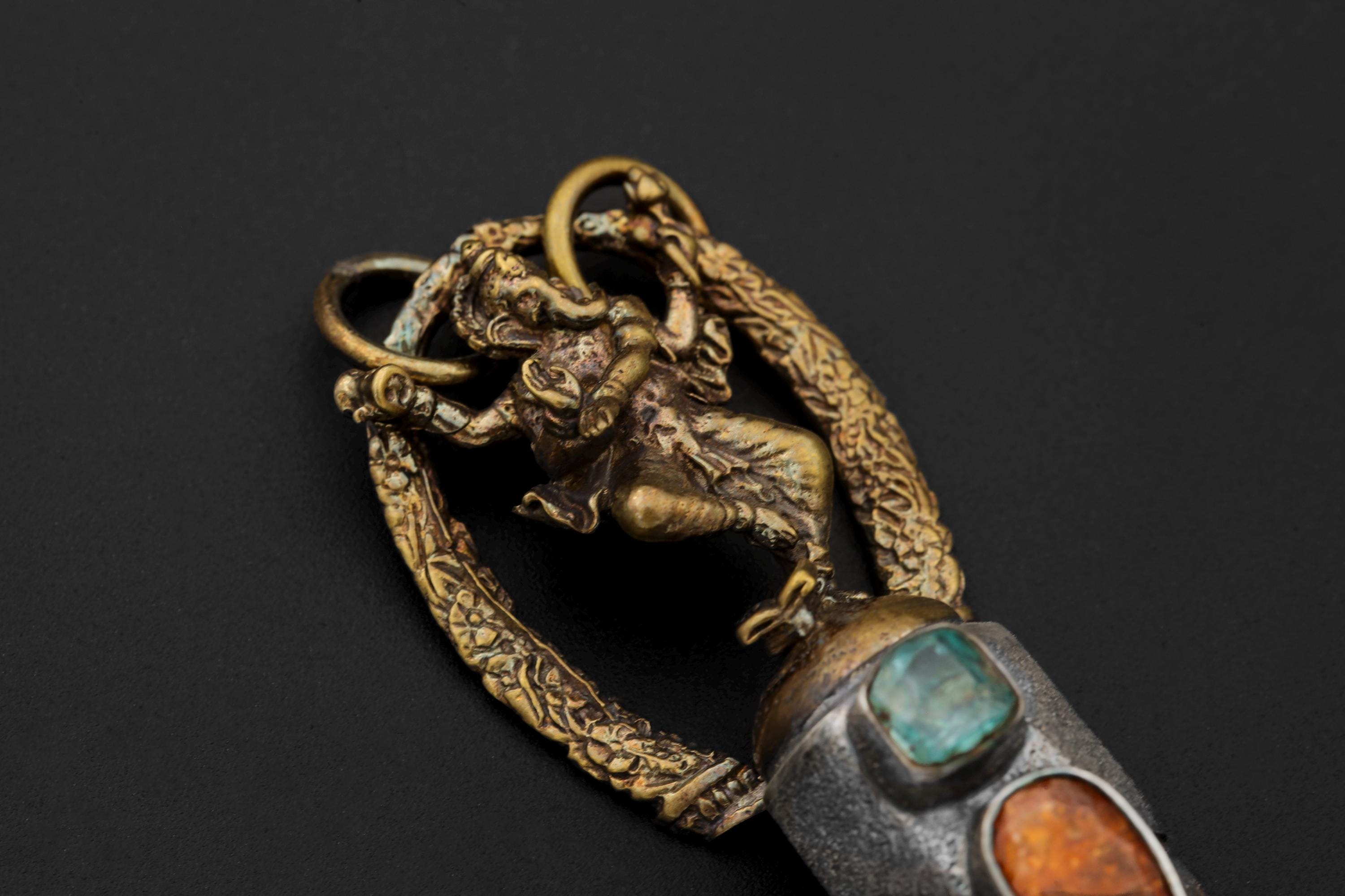 Pendant laid flat showing oxidized texture, gold plating luster, and clean symmetry between Ganesha figure and stones.