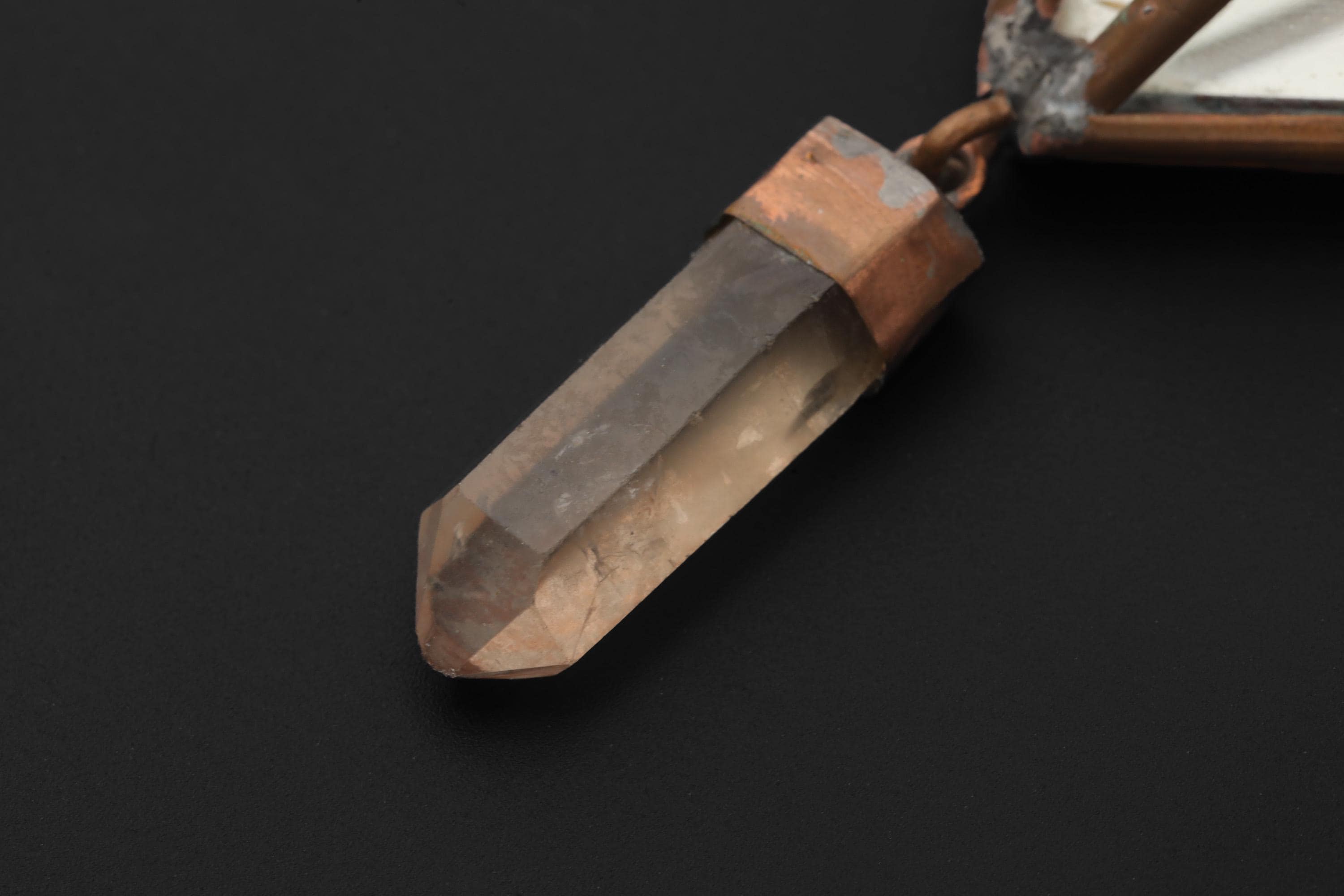 Close-up of raw Clear Quartz point suspended from copper and mirror glass hanging decoration.