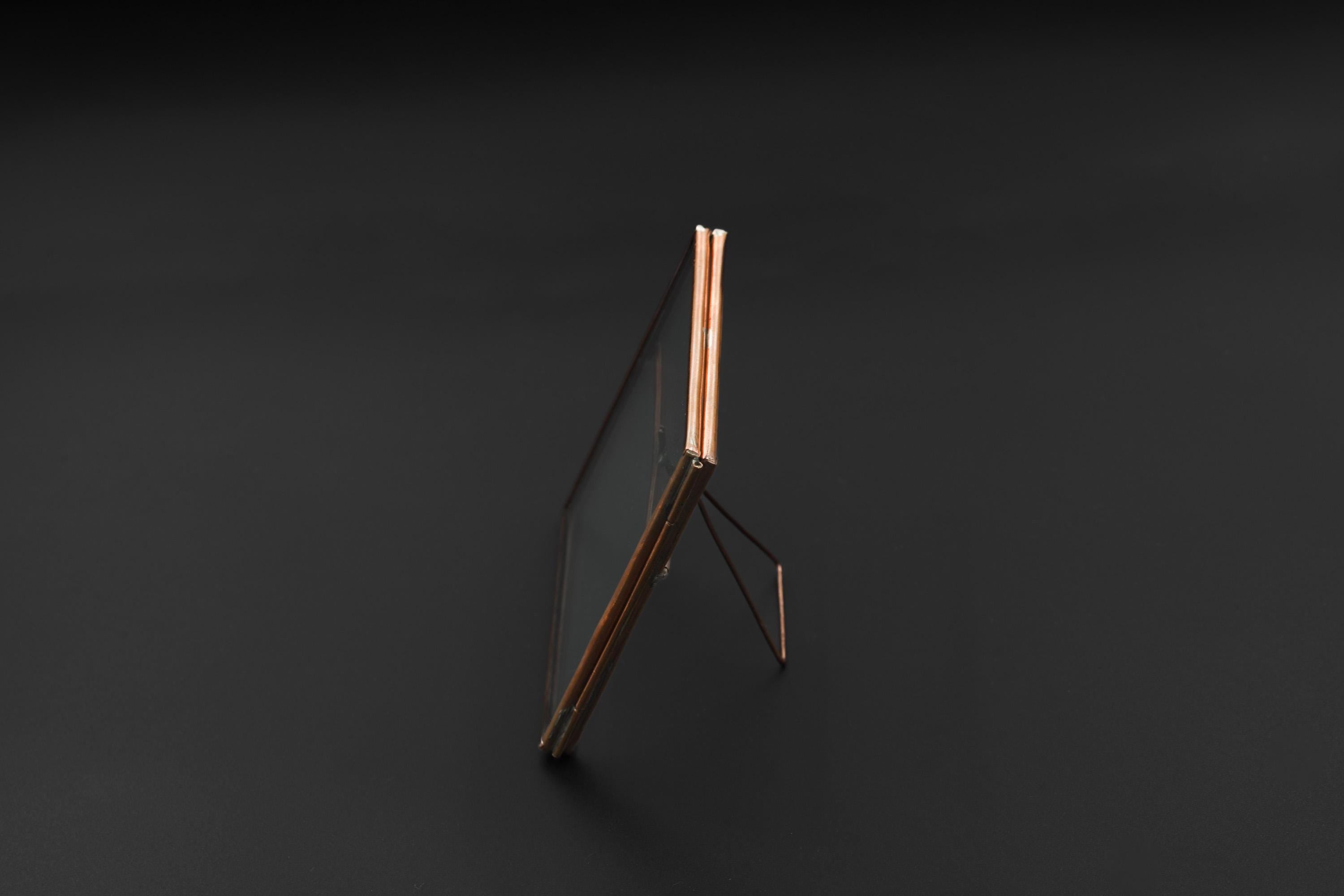 Copper glass photo frame shown on dark background with square shape, slim copper edging, and back stand.