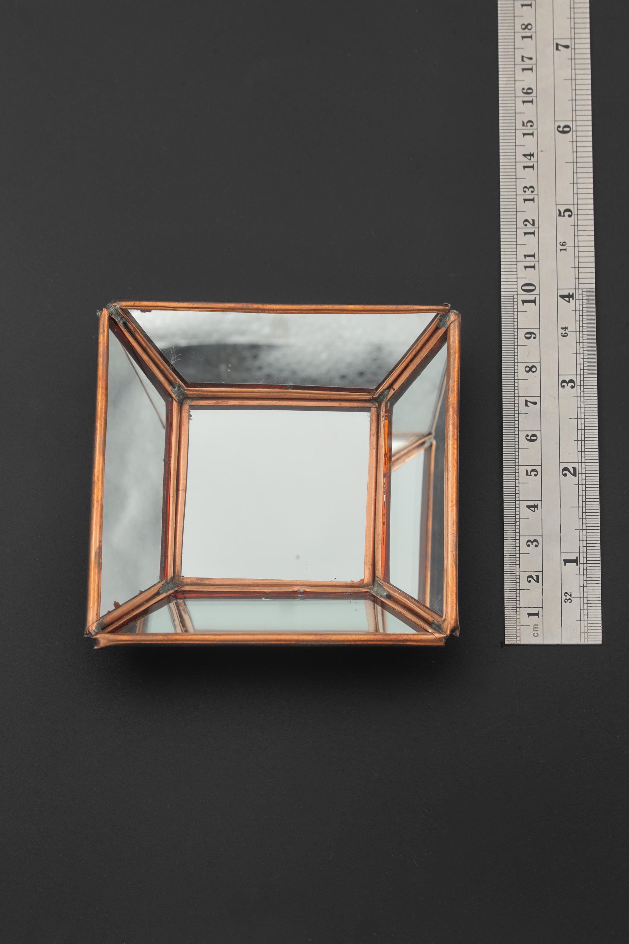 Square copper mirror shown beside a ruler for scale, with warm copper frame and reflective glass panels.