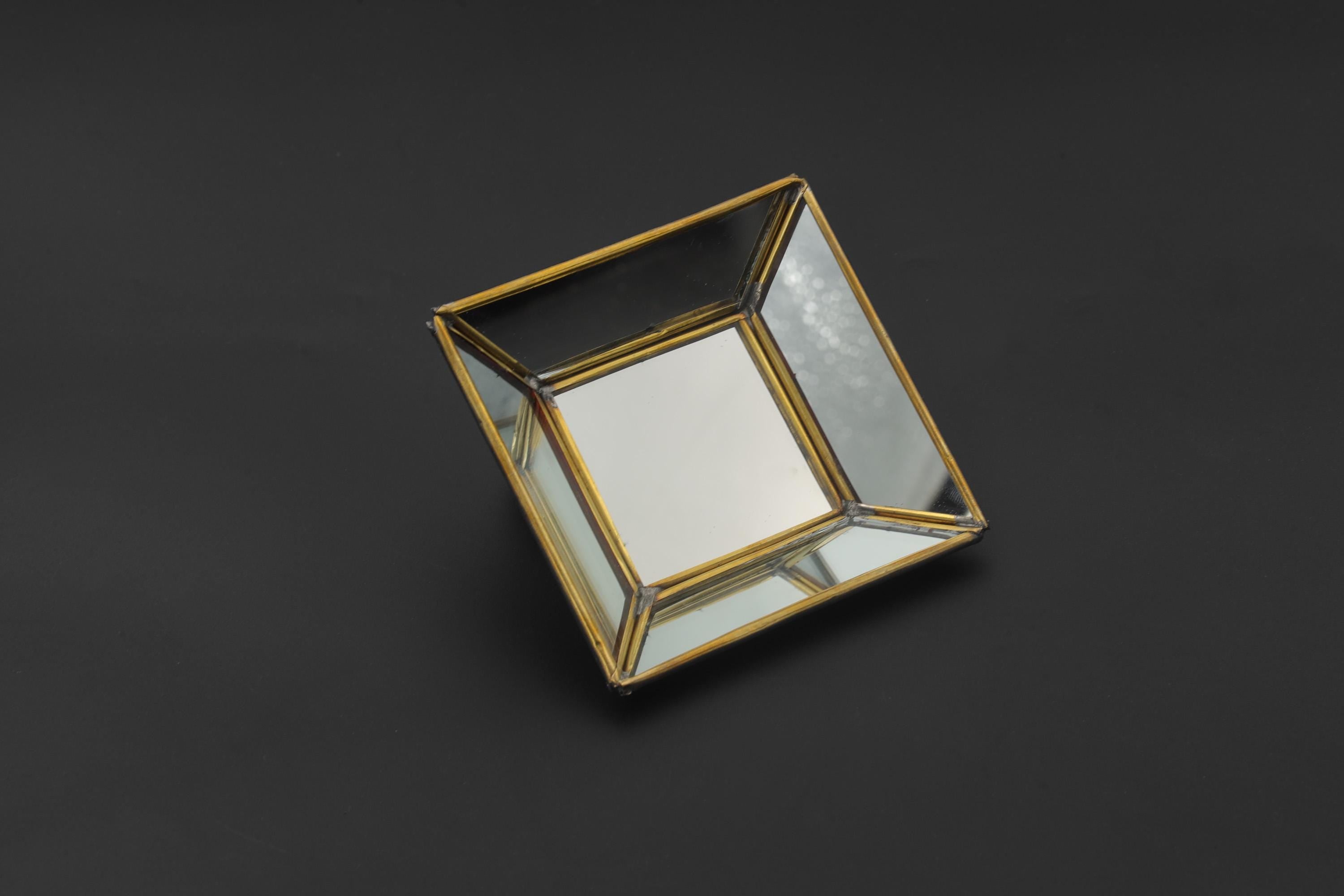Brass geometric mirror tray shown on dark background with pyramid-style reflective glass panels and square shape.