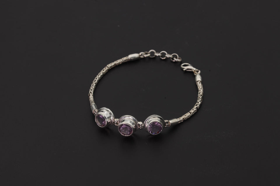 Amethyst bracelet displayed on dark background with three faceted purple stones and sterling silver Byzantine chain.