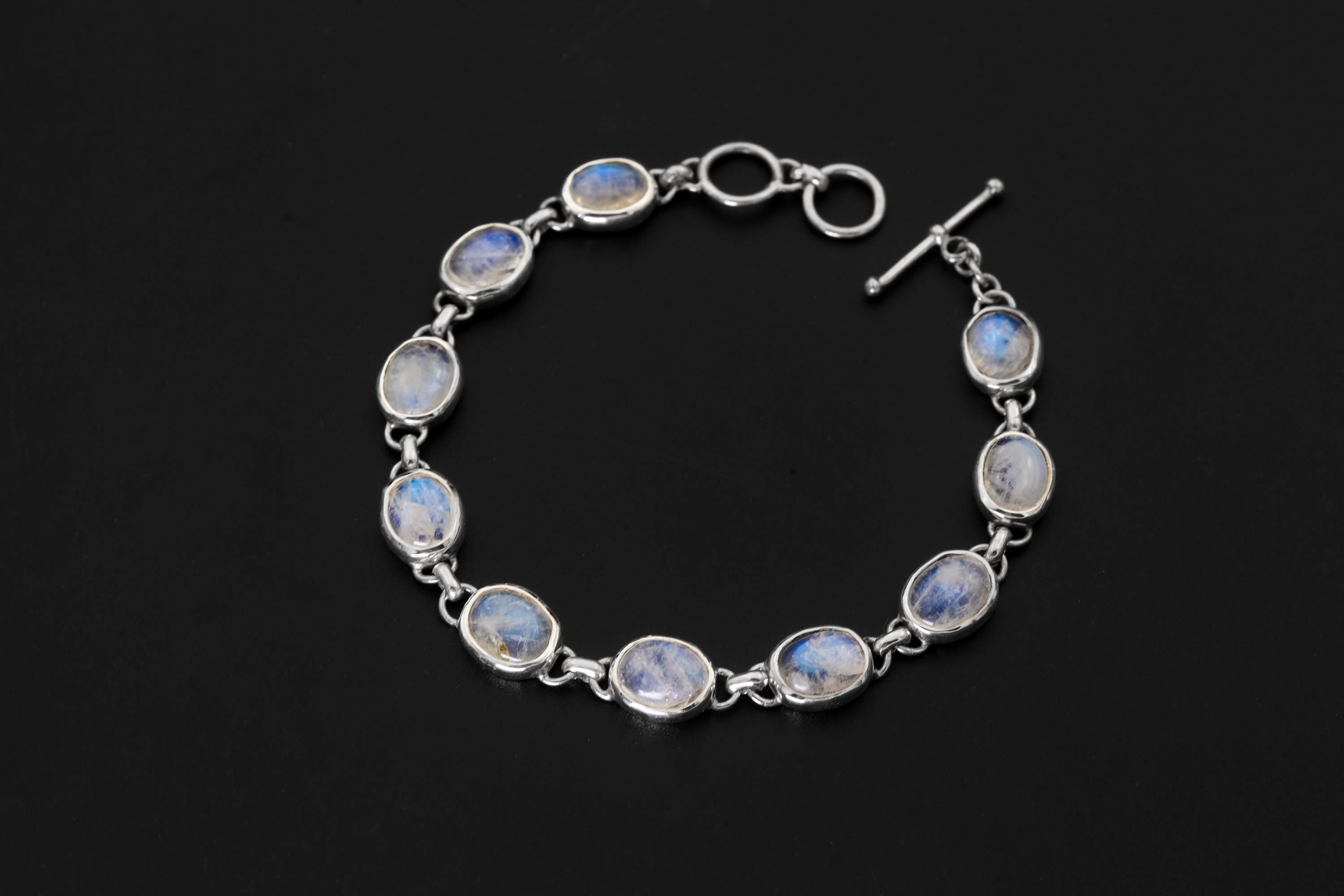 Blue Moonstone bracelet displayed on dark background with nine oval cabochons in polished sterling silver bezels.