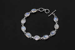 Blue Moonstone bracelet displayed on dark background with nine oval cabochons in polished sterling silver bezels.