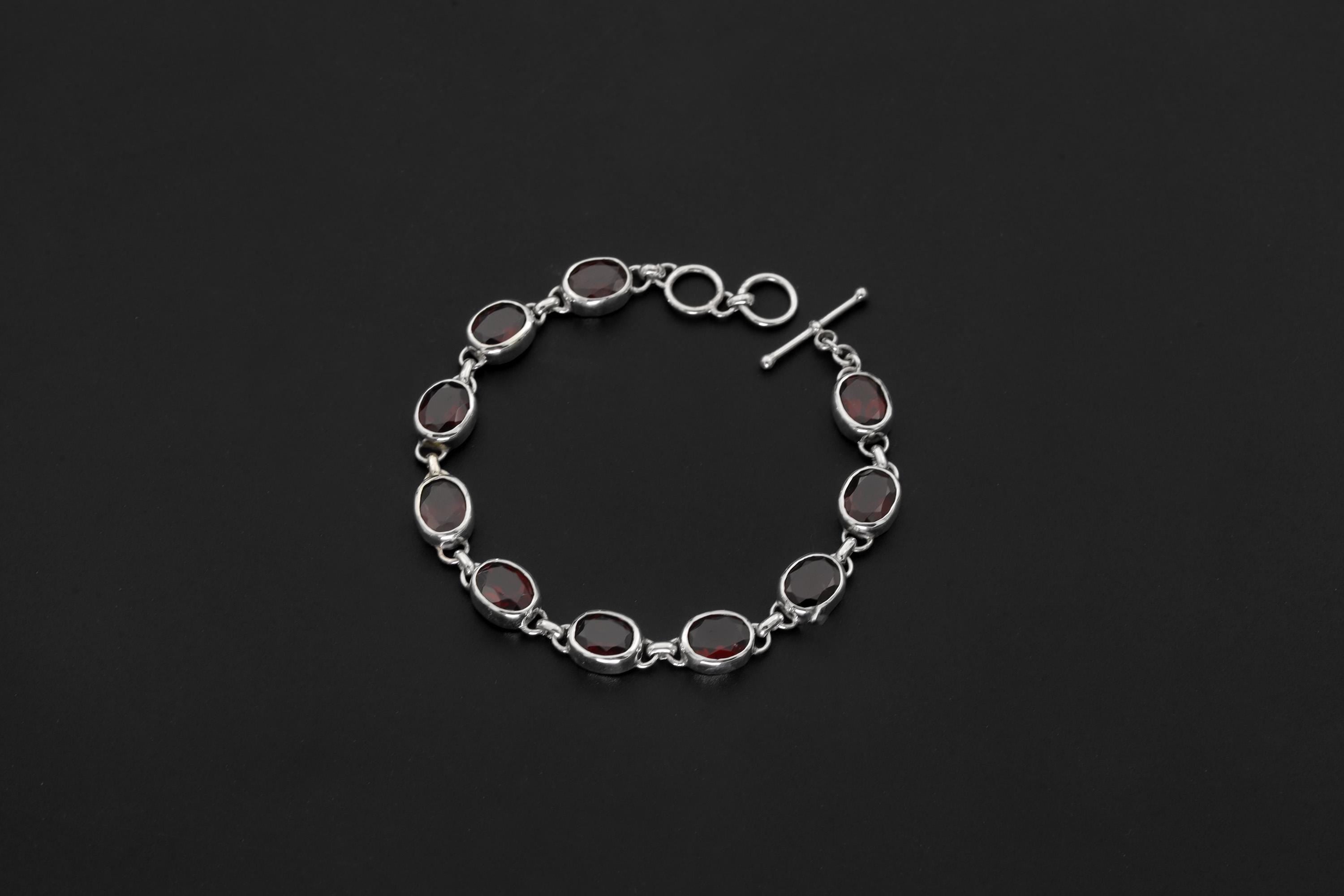 Garnet bracelet displayed on dark background with oval red gemstones in polished sterling silver bezels.
