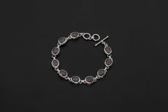 Garnet bracelet displayed on dark background with oval red gemstones in polished sterling silver bezels.