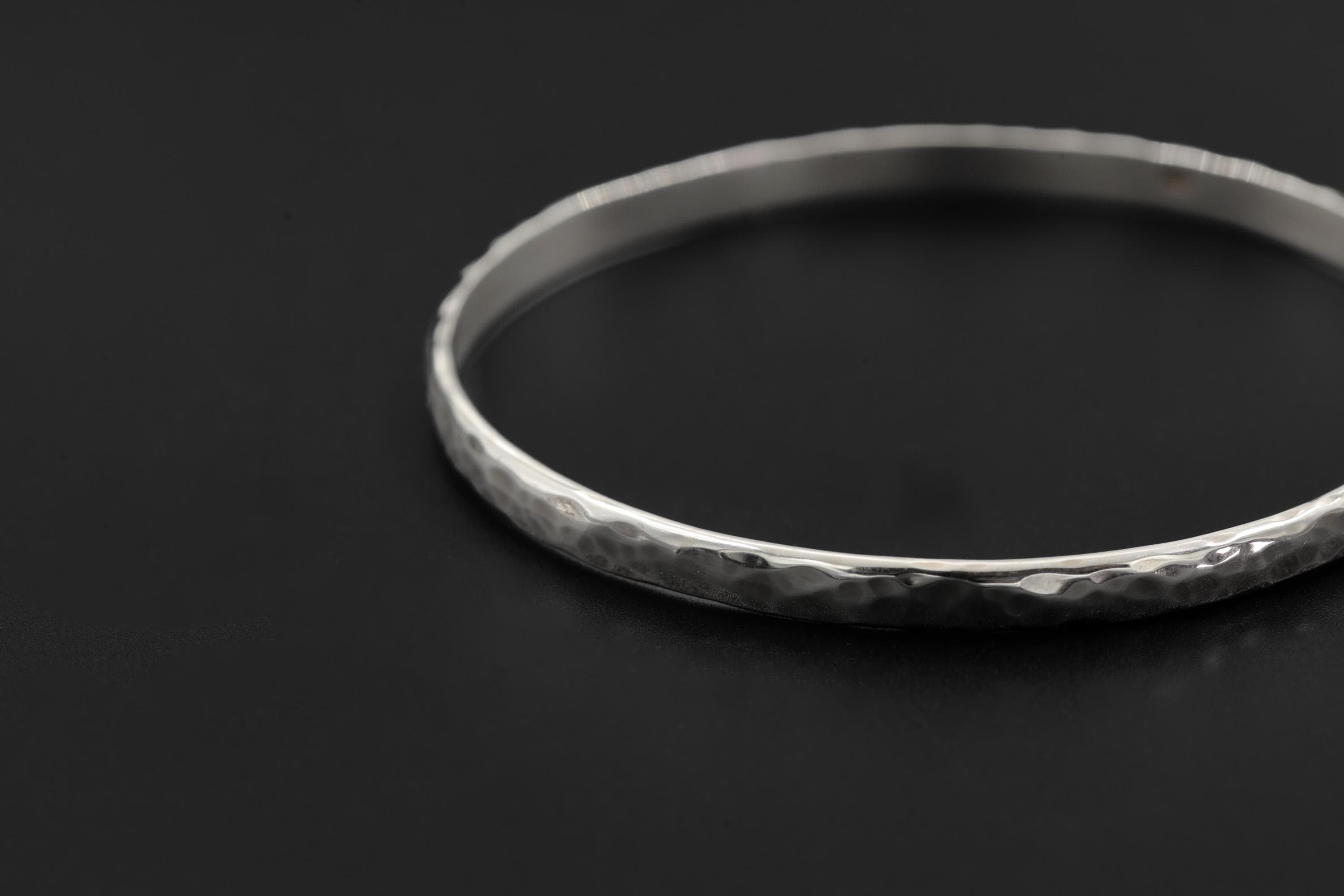 Close view of hammered silver bangle showing hand-textured surface and high-polish edge.