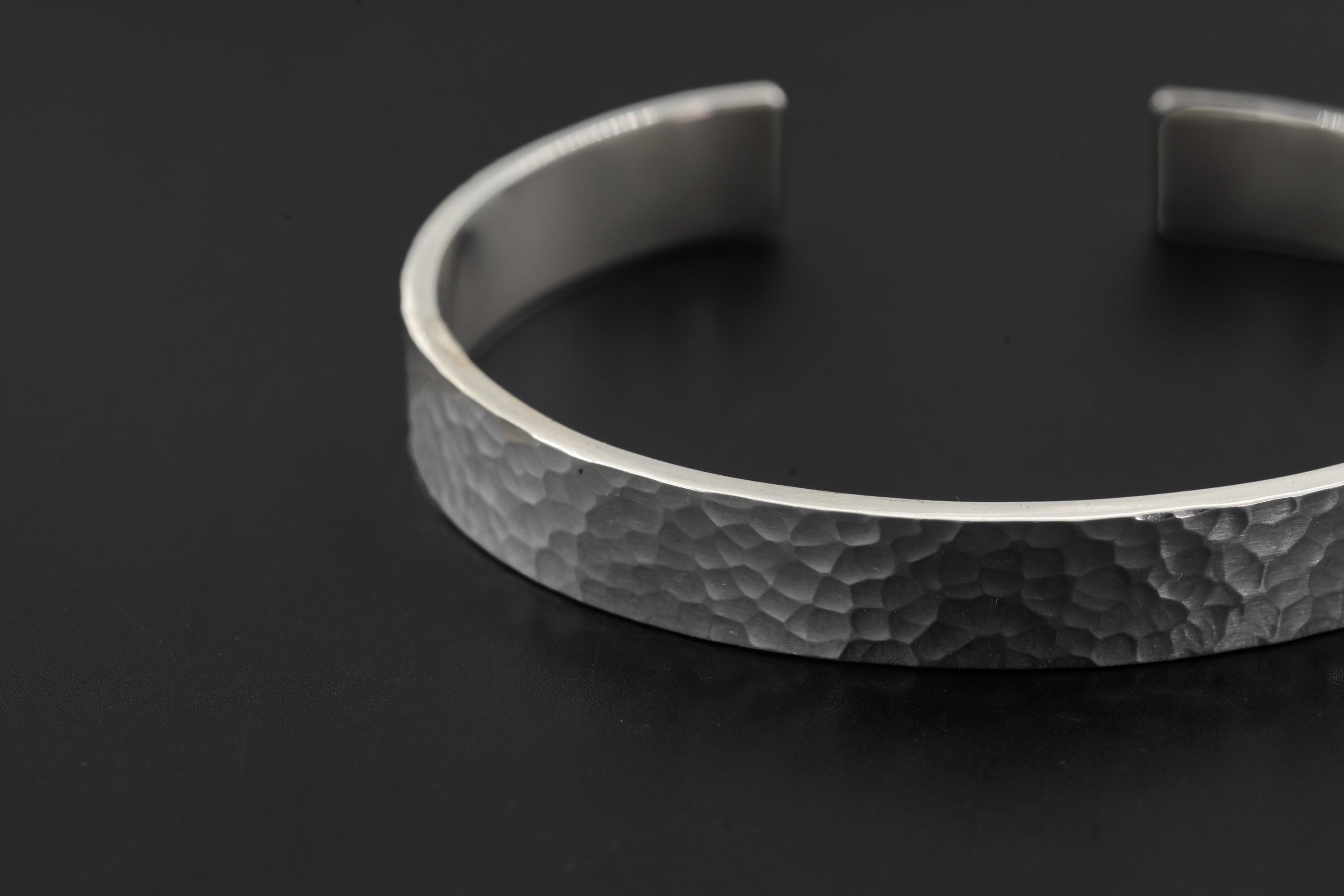 Close view of polished sterling silver bangle showing smooth surface and handmade silver structure.