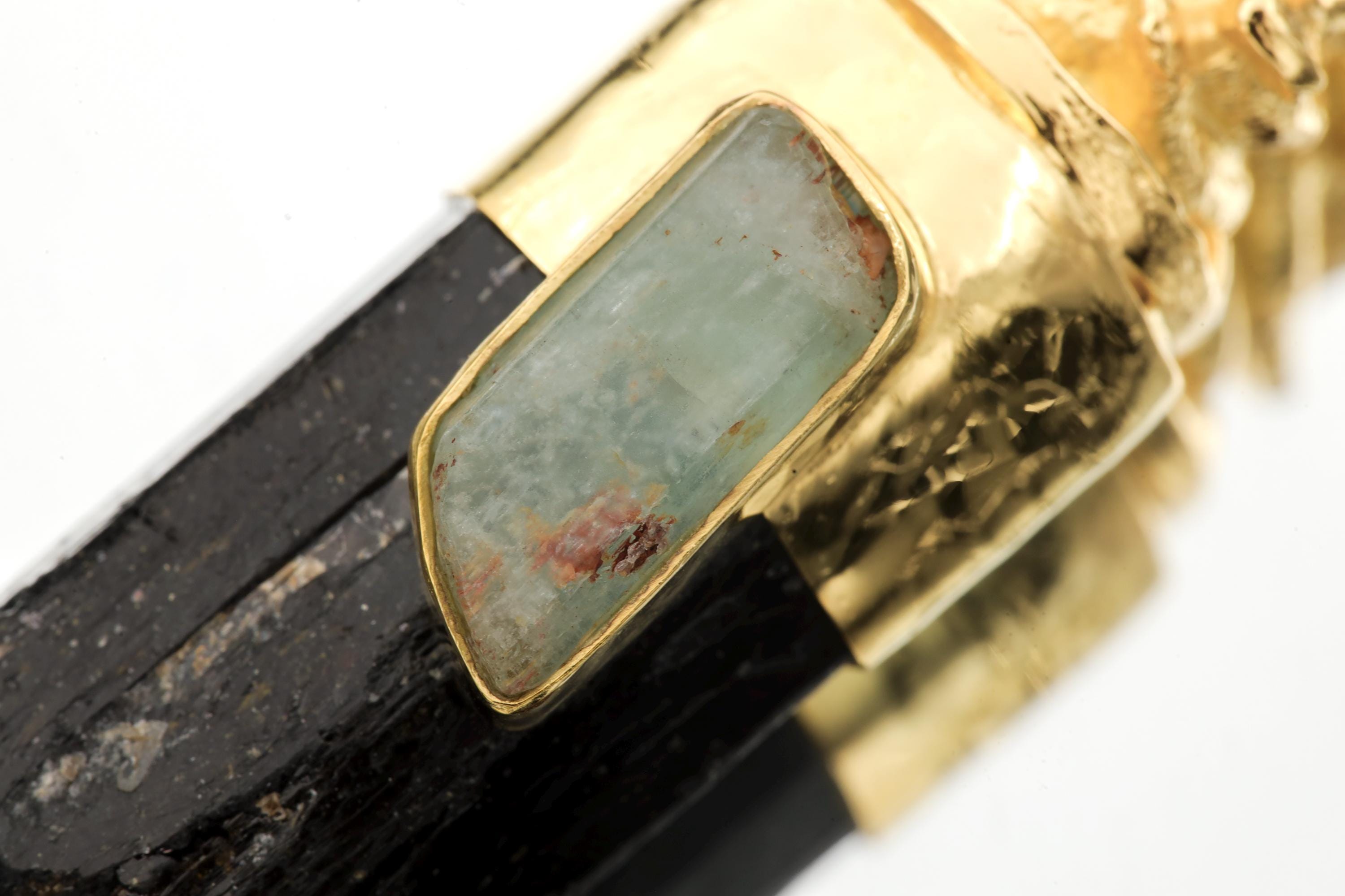 Close-up of Natural Australian Aquamarine Wand set in gold-plated sterling silver beneath a sacred brass figure.
