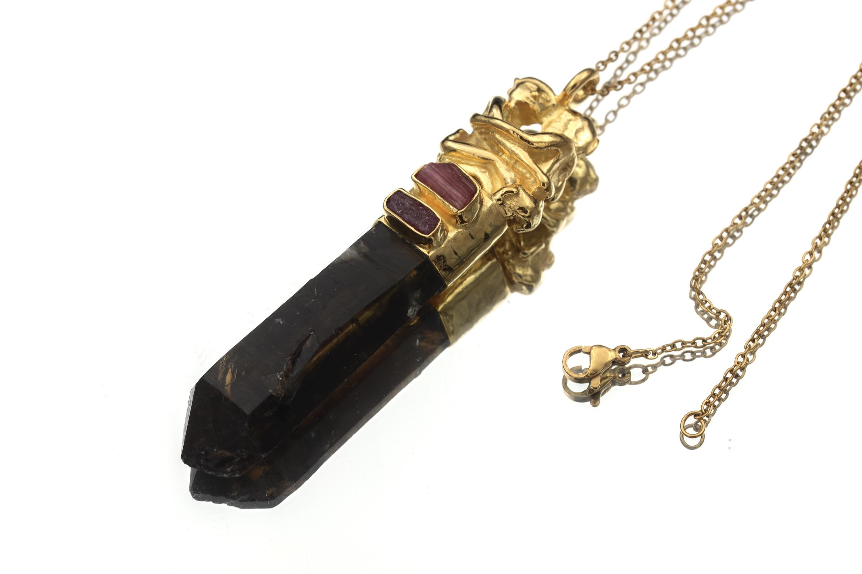 Lovers Triad Talisman shown on a dark background with gold-plated couple motif, Pink Tourmaline, Ruby, and Smoky Quartz.