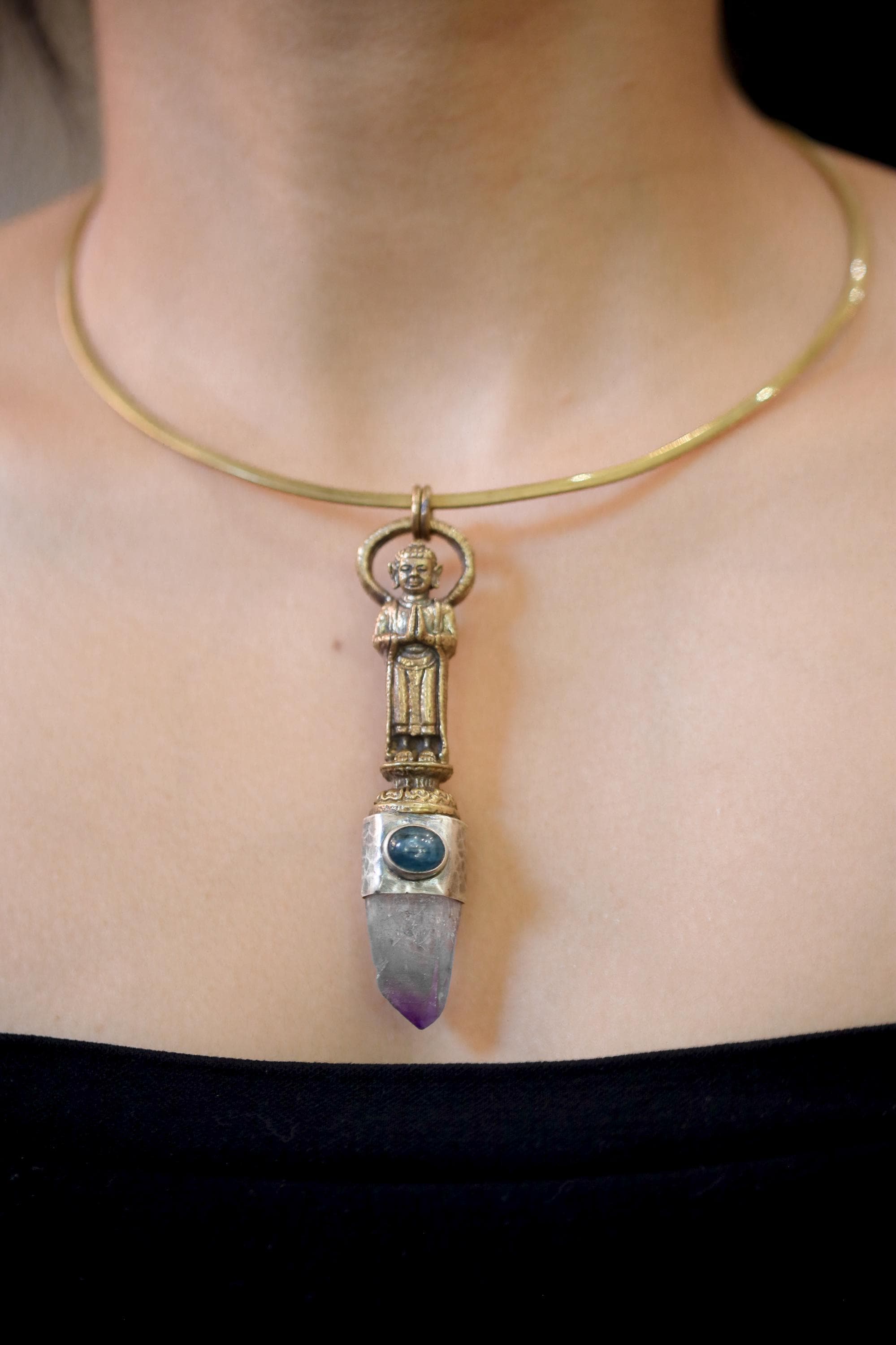 pendant on model neckline illustrating contrast between warm brass and cool-toned gemstones.