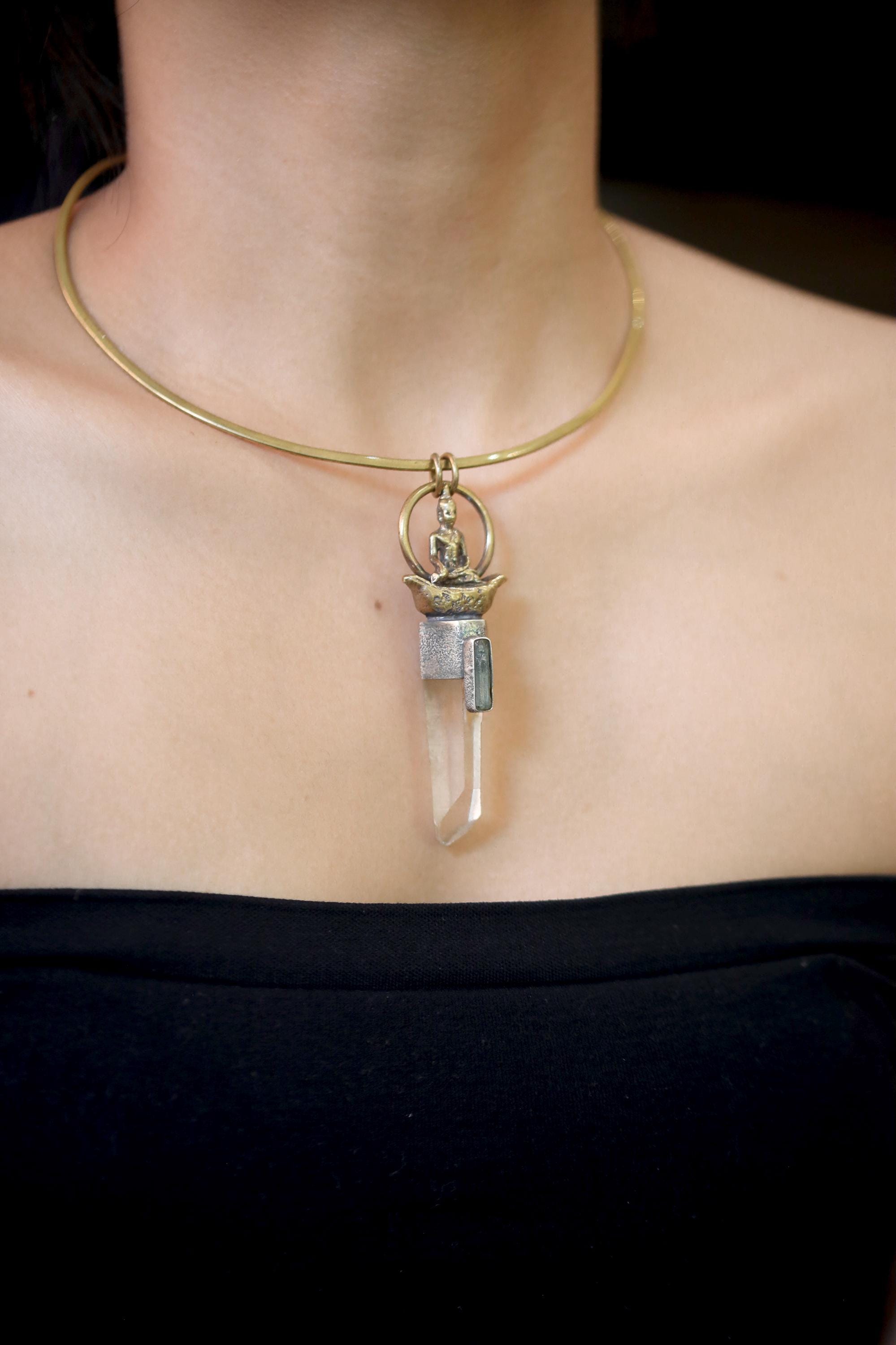 Pendant on model neckline under soft lighting emphasizing the spiritual motif and earthy metal contrast.