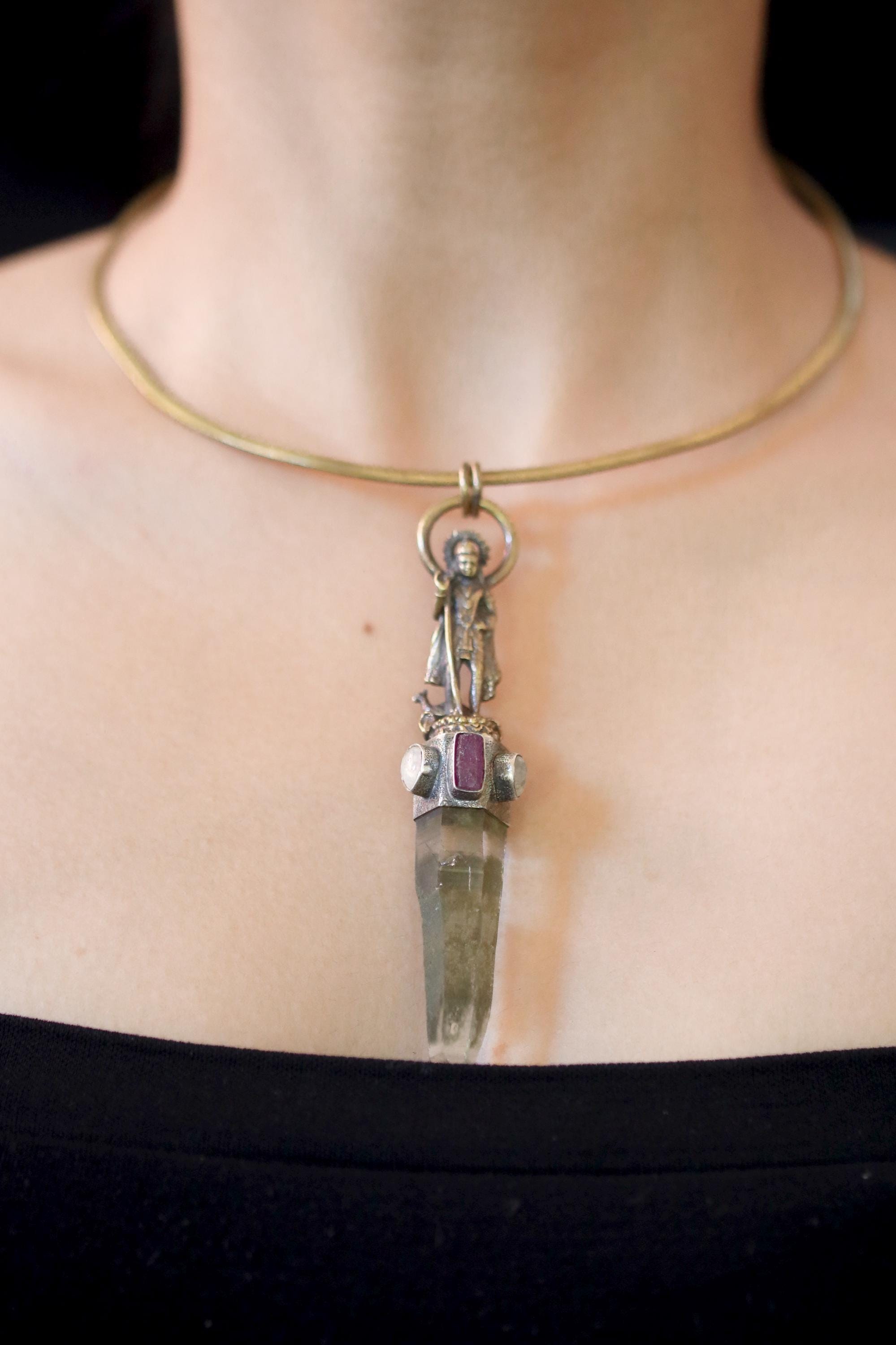 Pendant on model neckline under warm light highlighting harmony between brass, quartz, and gemstones.