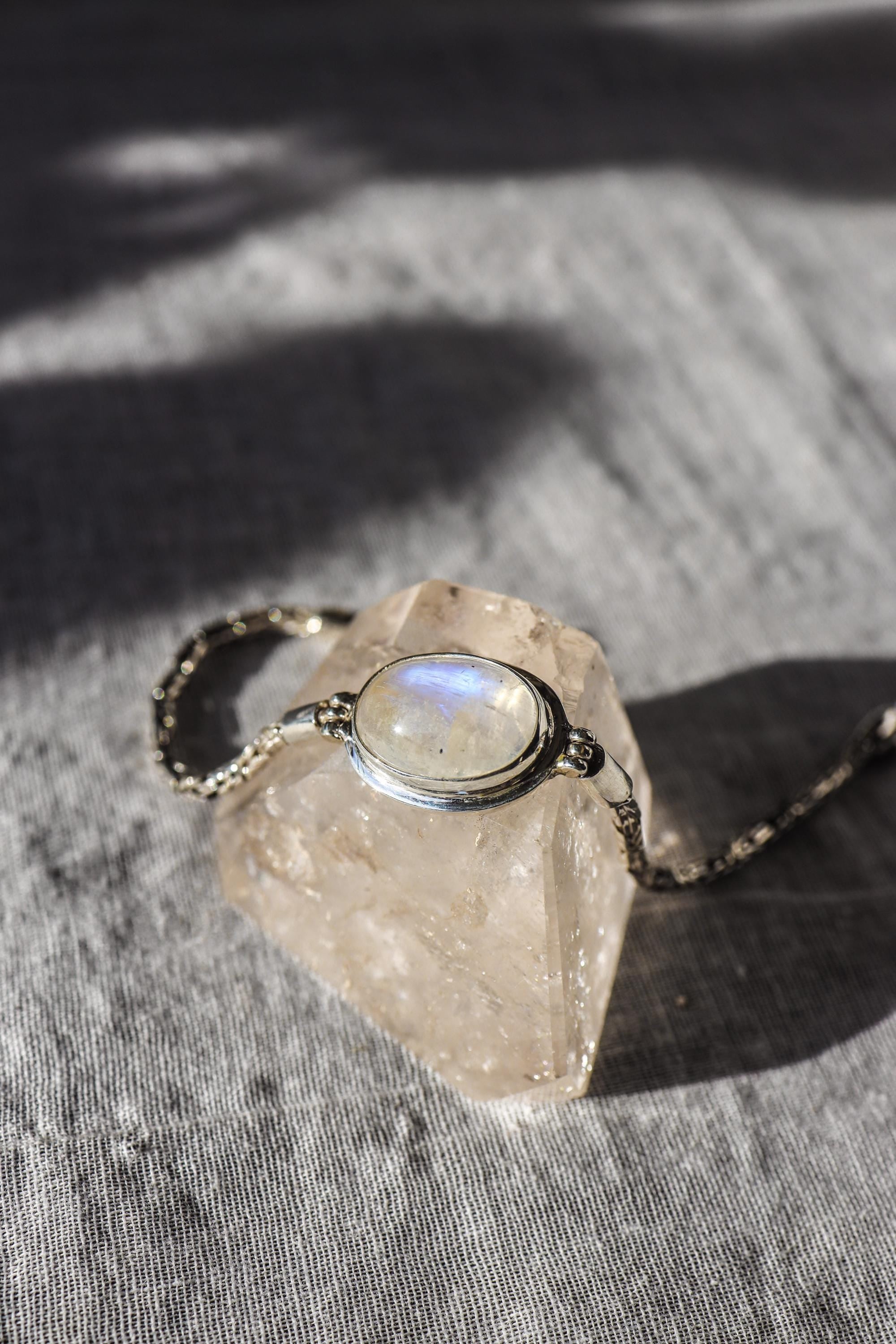 Blue Moonstone sterling silver bracelet shown on textured stone with polished bezel and woven chain detail.