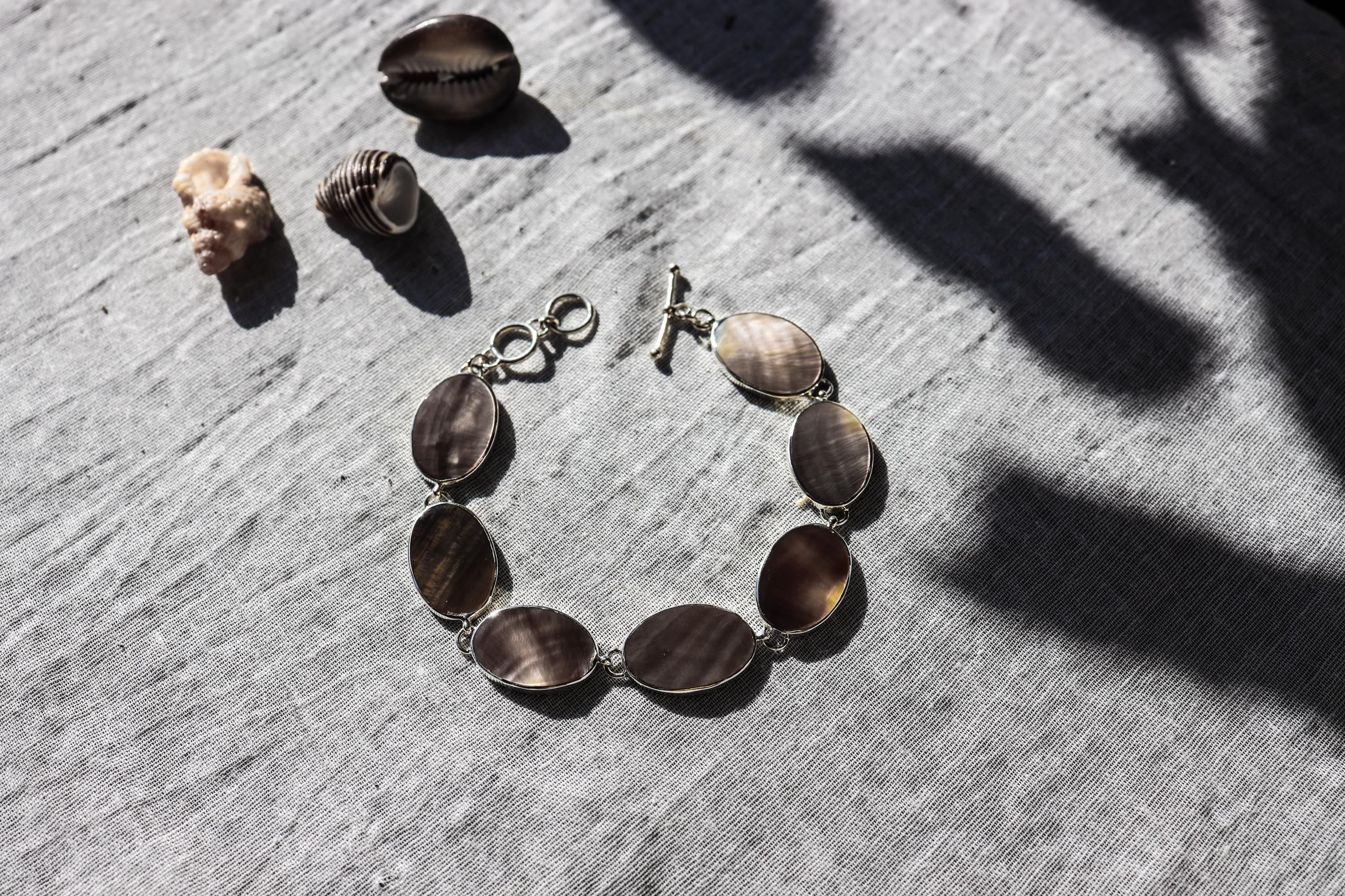 Mother of Pearl bracelet displayed on textured stone with natural oval shell cabochons and polished silver settings.