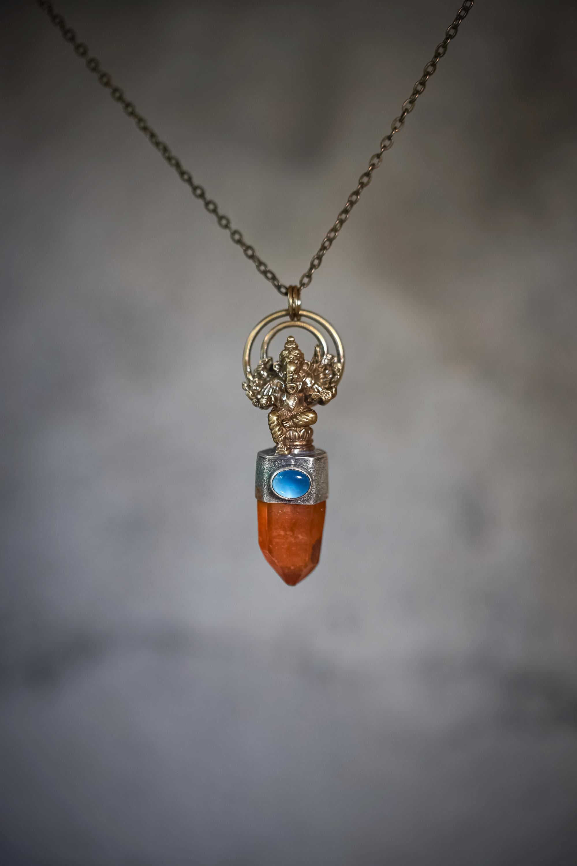 Pendant suspended against a gradient background showing light reflection on quartz facets and brass cast finish.