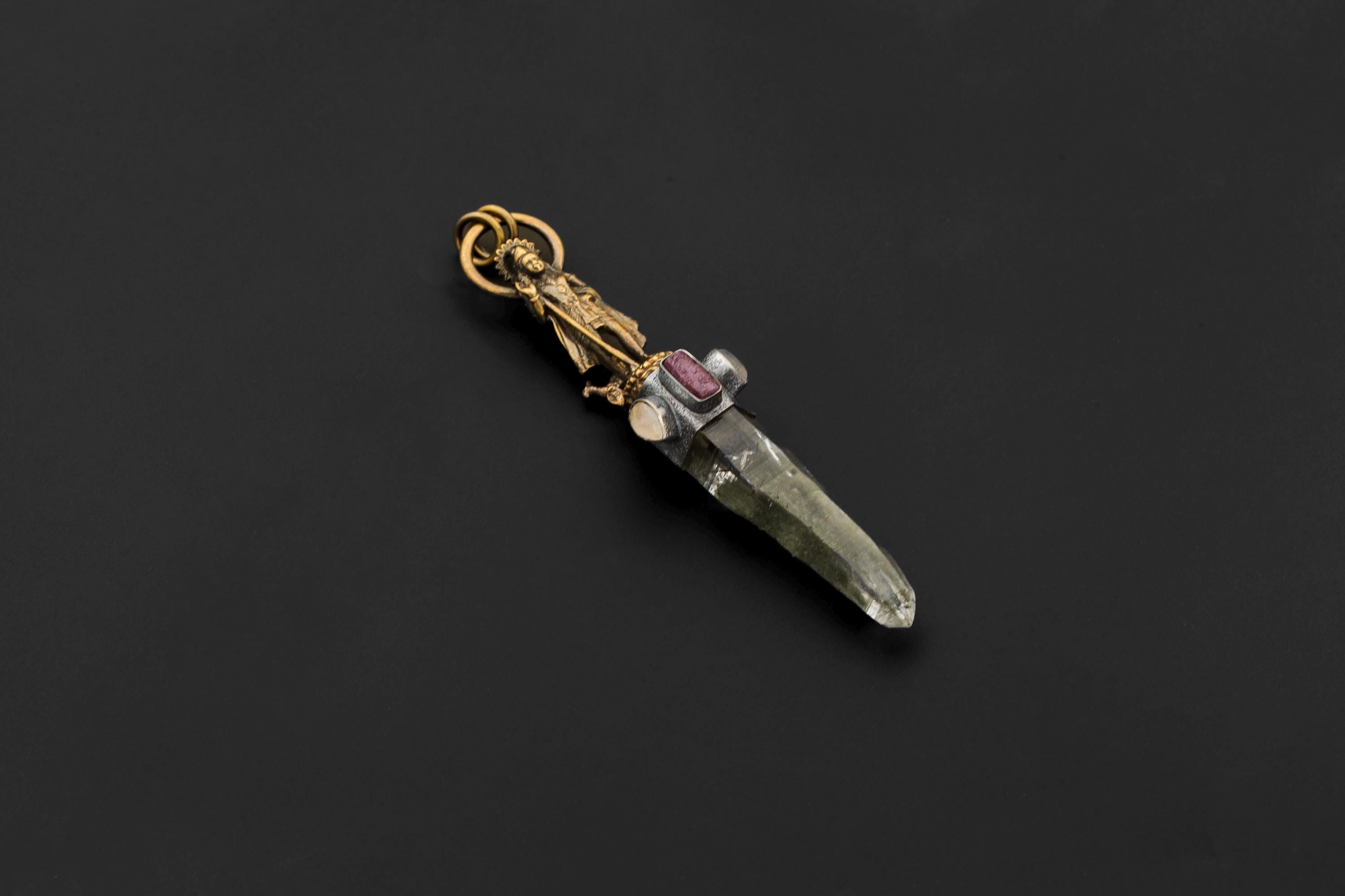 Pendant laid flat on black surface showing full composition from Saraswati figure to quartz termination with visible striations.