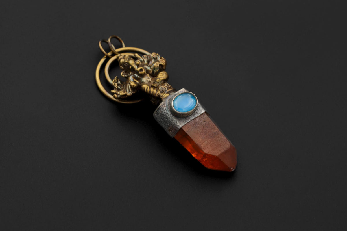 Ganesha Talisman pendant on black background featuring brass-cast Ganesha figure, Australian Lithium Finger Quartz point, and blue Aquamarine cabochon set in oxidized silver bezel.