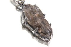 Tibetan Double Terminated Quartz pendant on white background showing internal carbon inclusions and oxidized silver claws.