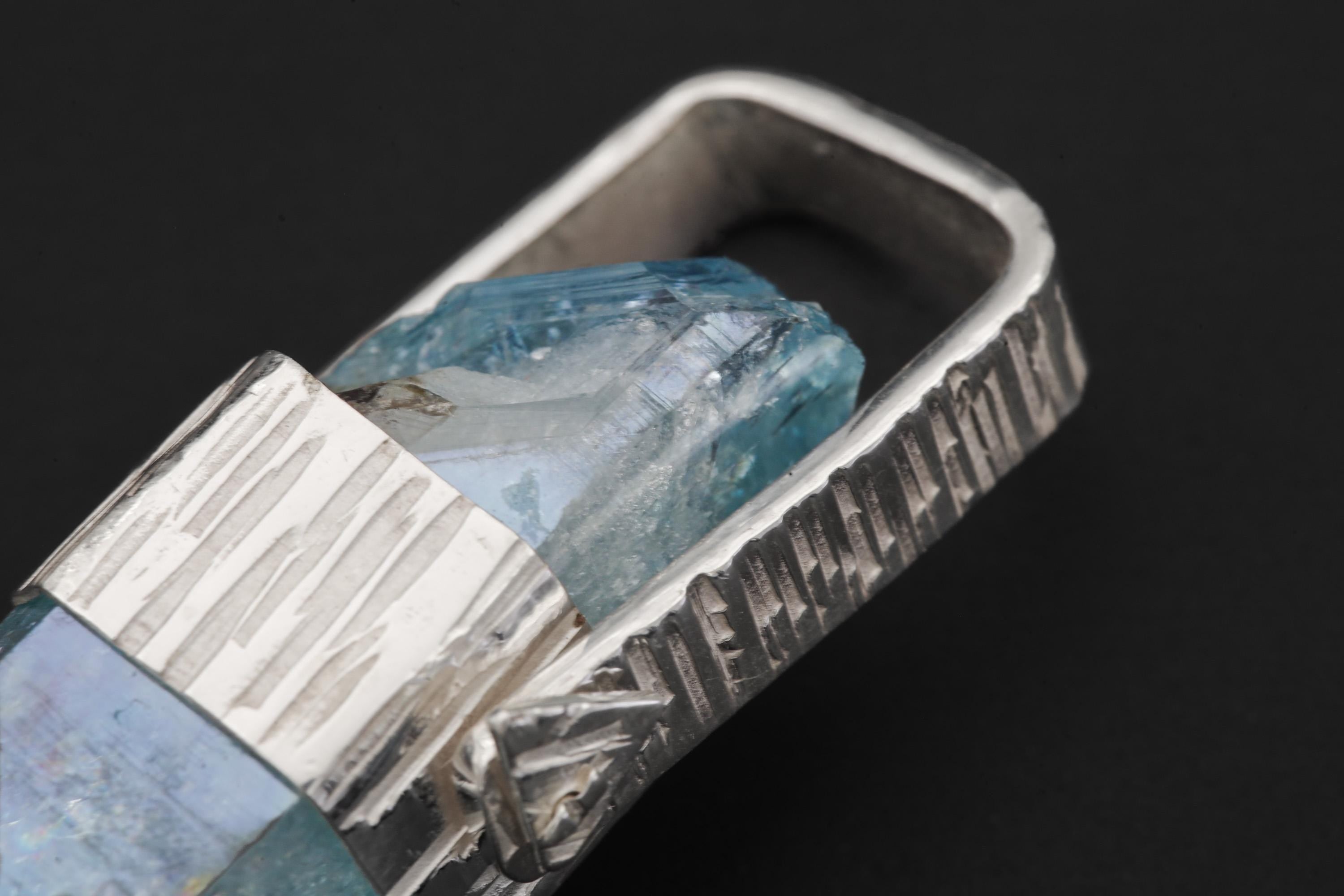 Close-up of Aqua Aura Quartz pendant showing blue crystal point, line-hammered silver wrap, and wide triangular bail.