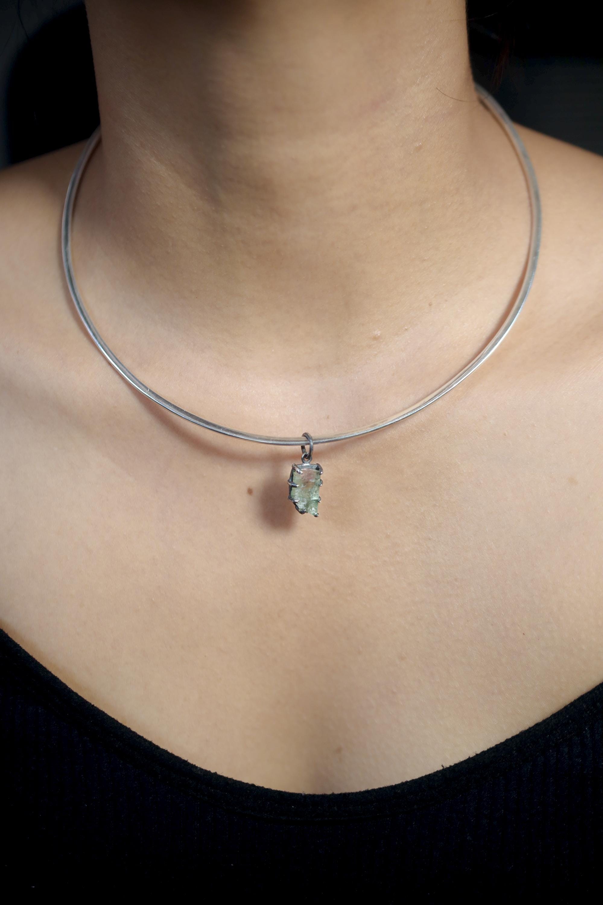 Model wearing green tourmaline pendant on silver choker necklace showing natural light reflection.