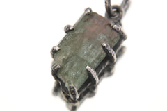 Close-up of green tourmaline pendant held between fingers showing natural crystal striations.