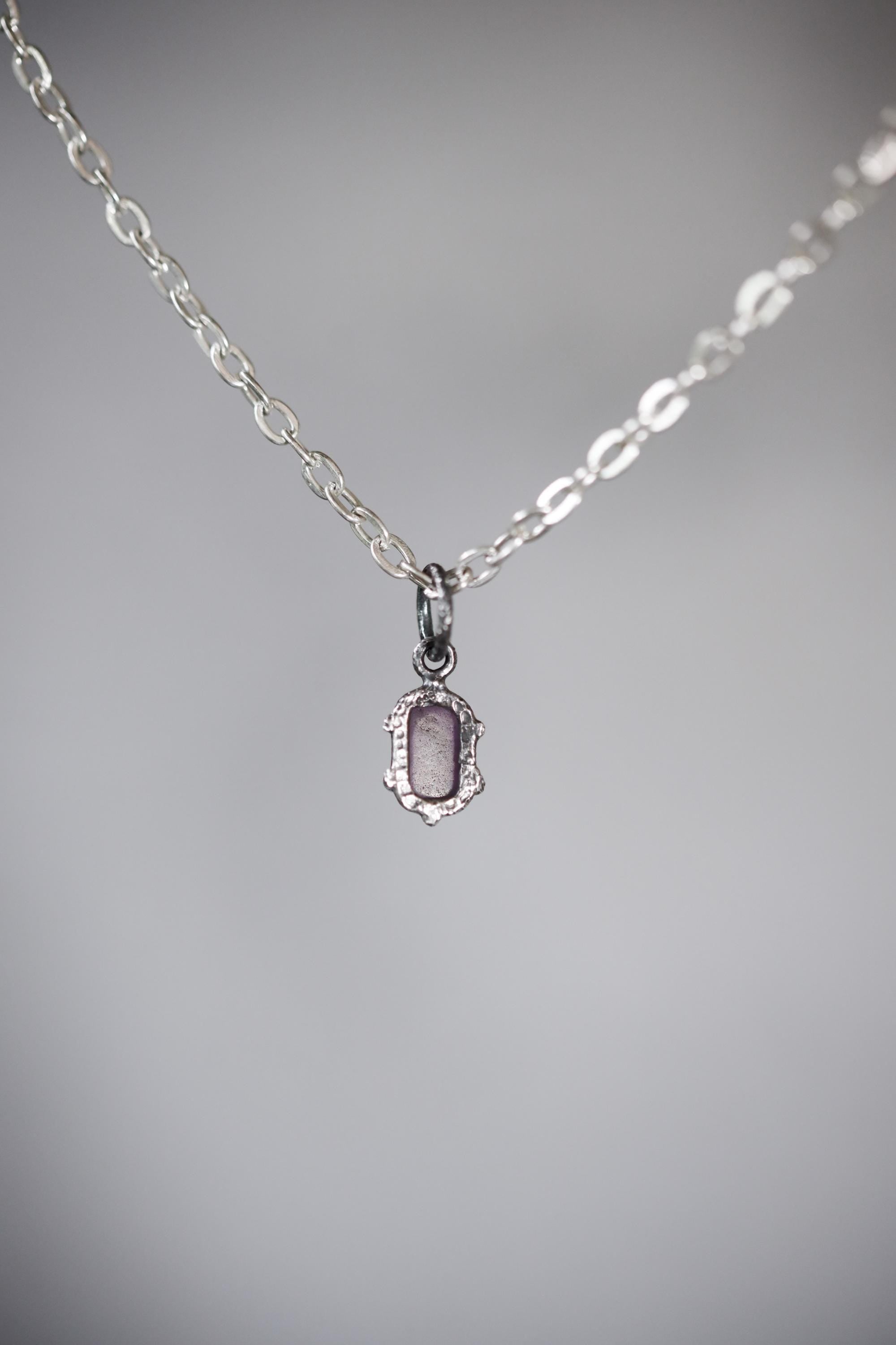 Amethyst cube pendant on grey background showing oxidized sterling silver claws and compact violet gemstone form.