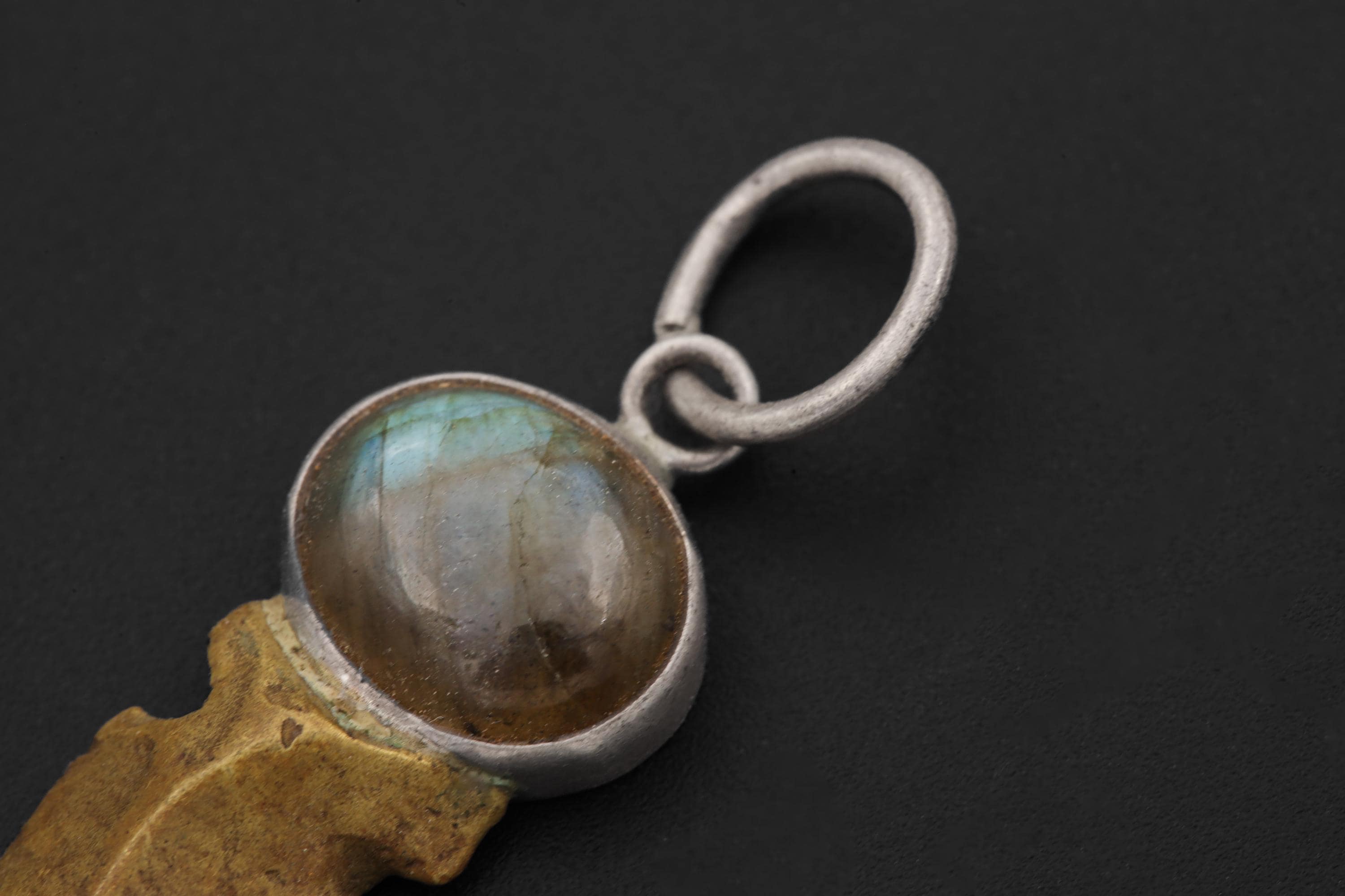 Close view of Labradorite cabochon above brass Obsidian spearhead pendant on textured stone.