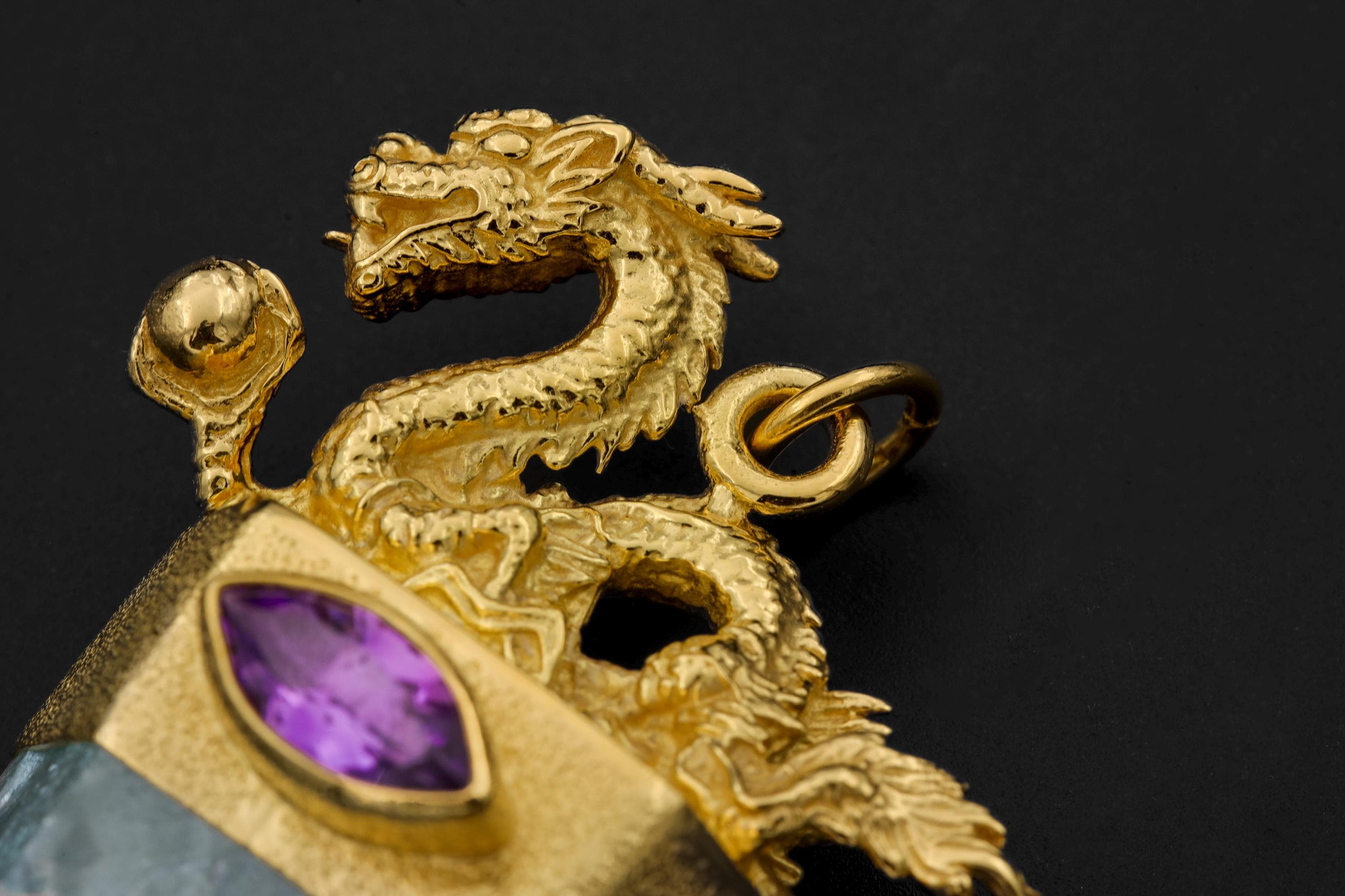 Close-up of cast brass dragon crest and faceted Amethyst eye in a high-polish 18k gold-plated pendant.