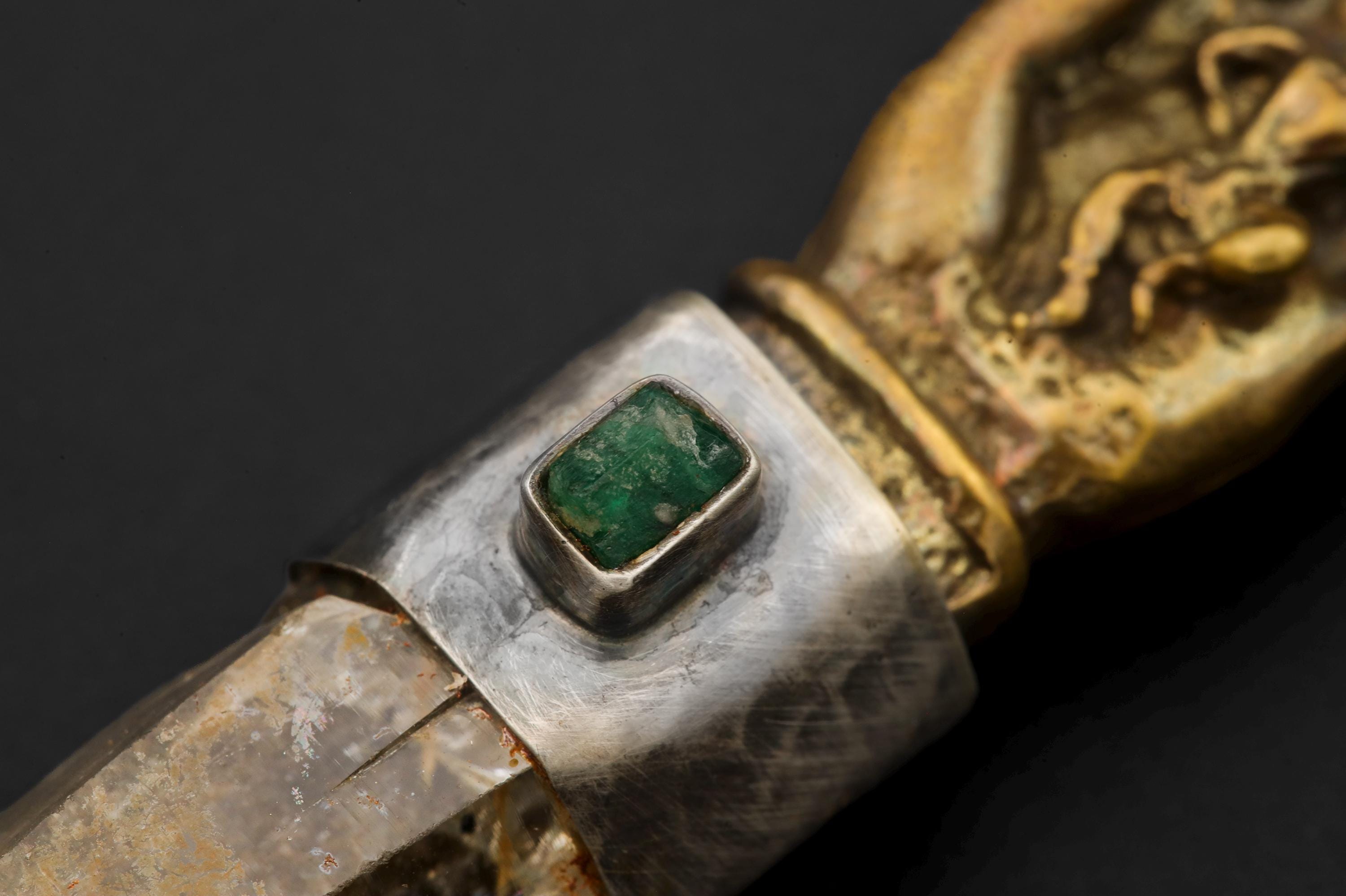 Side view macro of oxidized silver bezel surrounding emerald with visible texture and aged patina.

Pendant photographed horizontally on black background showing entire shape from brass hand top to quartz termination point.