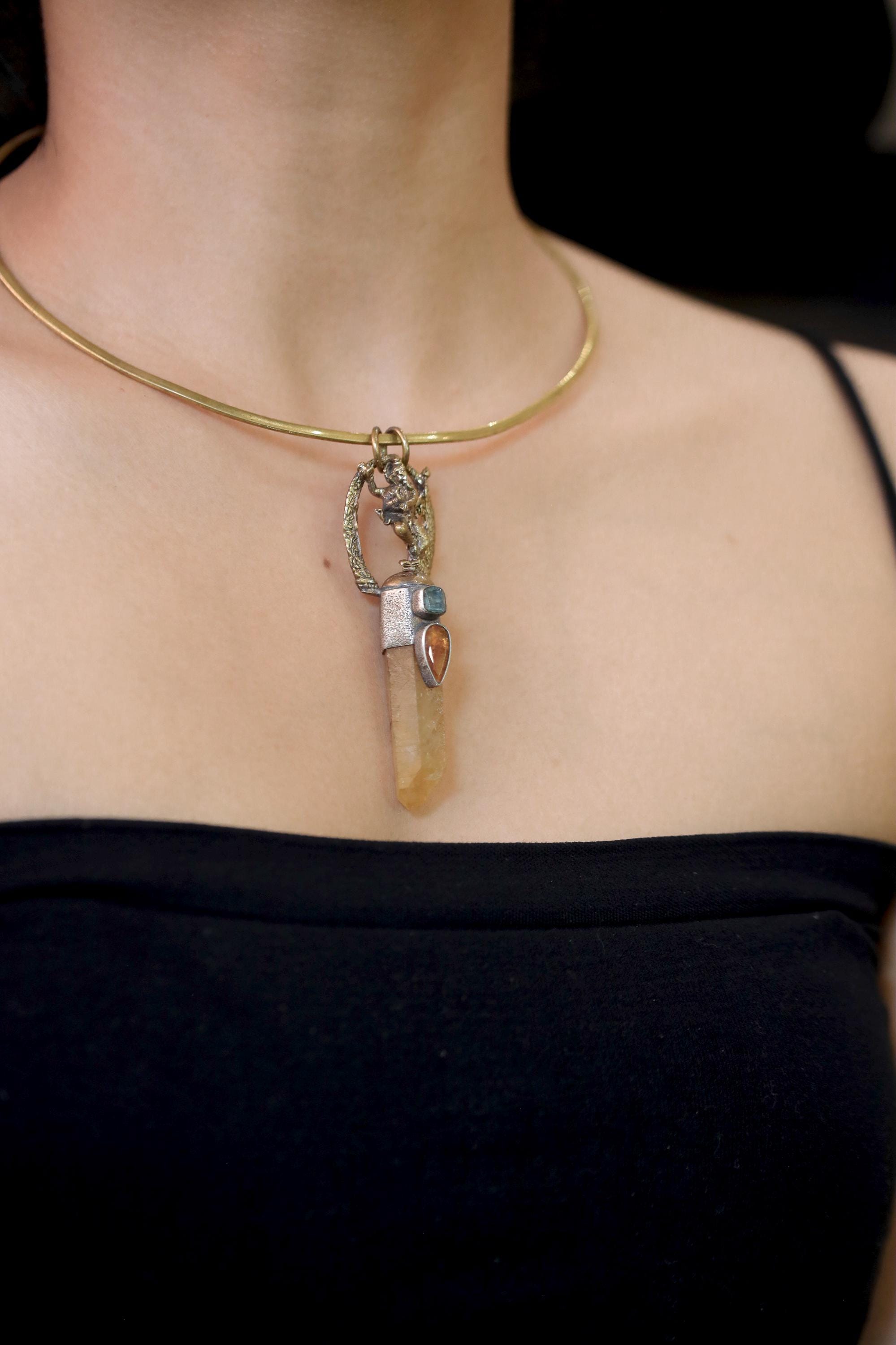 Side angle close-up of faceted orange Kyanite stone and raw blue-green Apatite inclusion framed in silver.