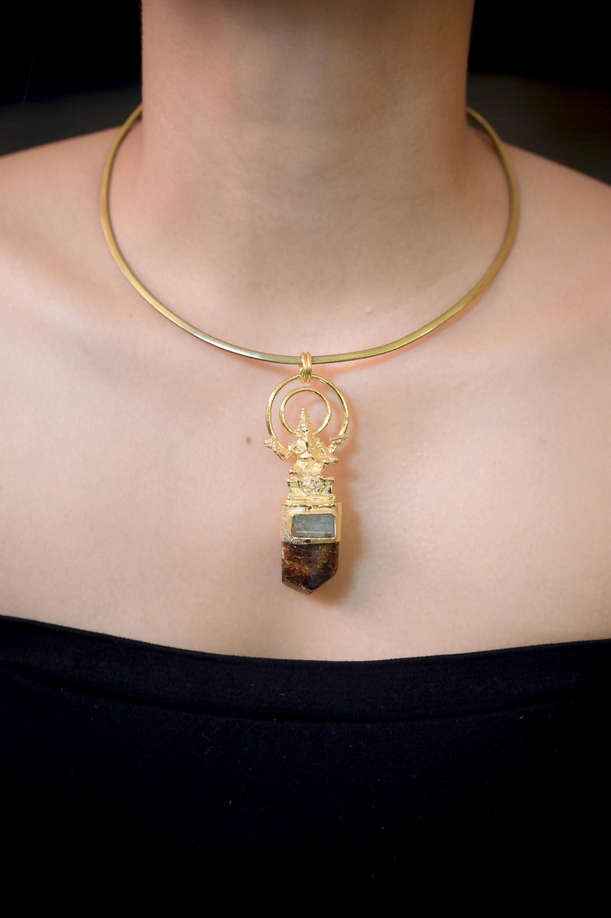 Lord Ganesha Talisman Pendant on white background featuring intricate gold-plated brass Ganesha figure above natural Brown Dravite Tourmaline crystal and square-cut Aquamarine set in 925 sterling silver bezel.