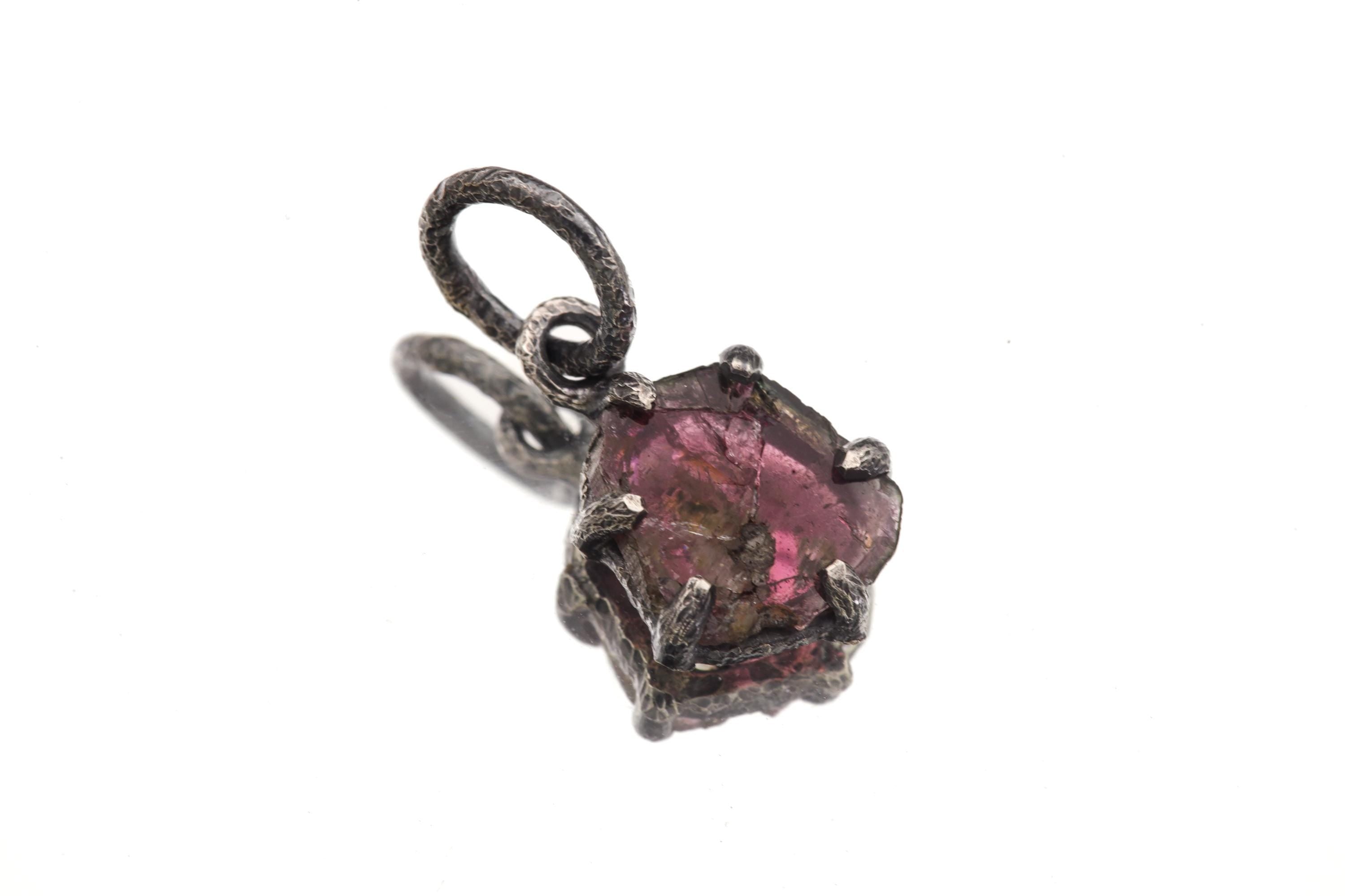 Pink Tourmaline Rubellite pendant on white background showing organic stone shape, darker rind, and textured silver bail.