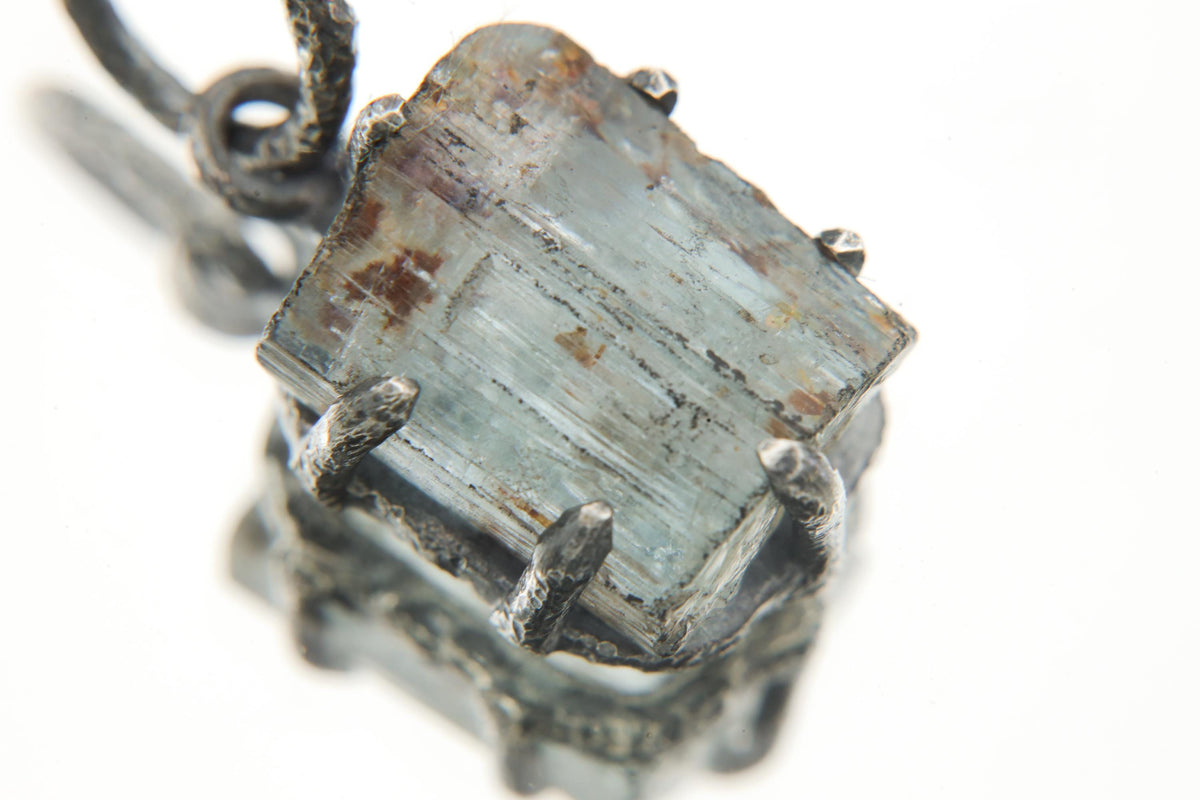 Close-up of Australian Raw Gem Aquamarine wand pendant in oxidized sterling silver claw setting with pale blue-green crystal.