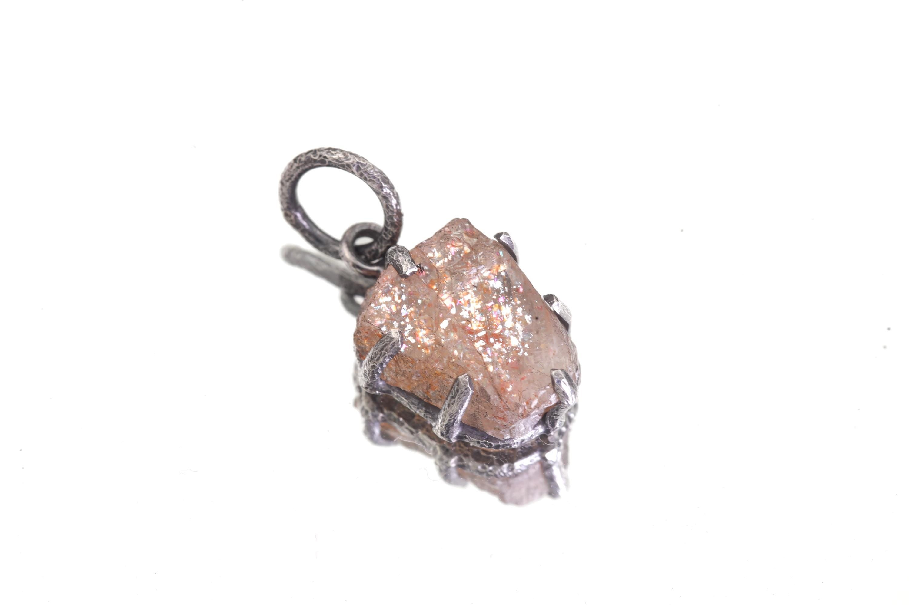 Sunstone pendant shown on sterling silver chain with grey background, featuring small claw-set orange-brown stone.